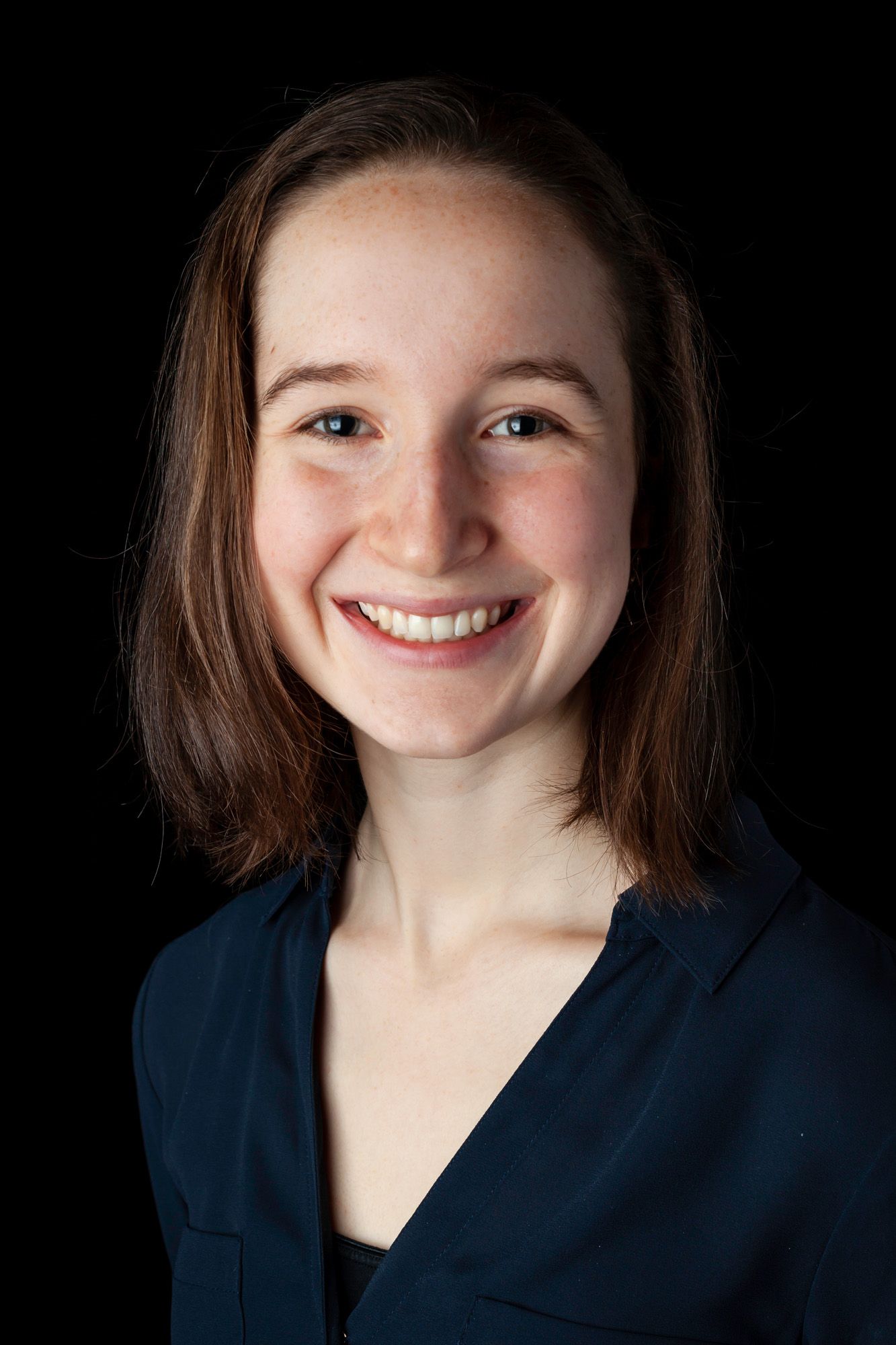 This portrait shows a smiling individual with shoulder-length hair, wearing a dark blue shirt