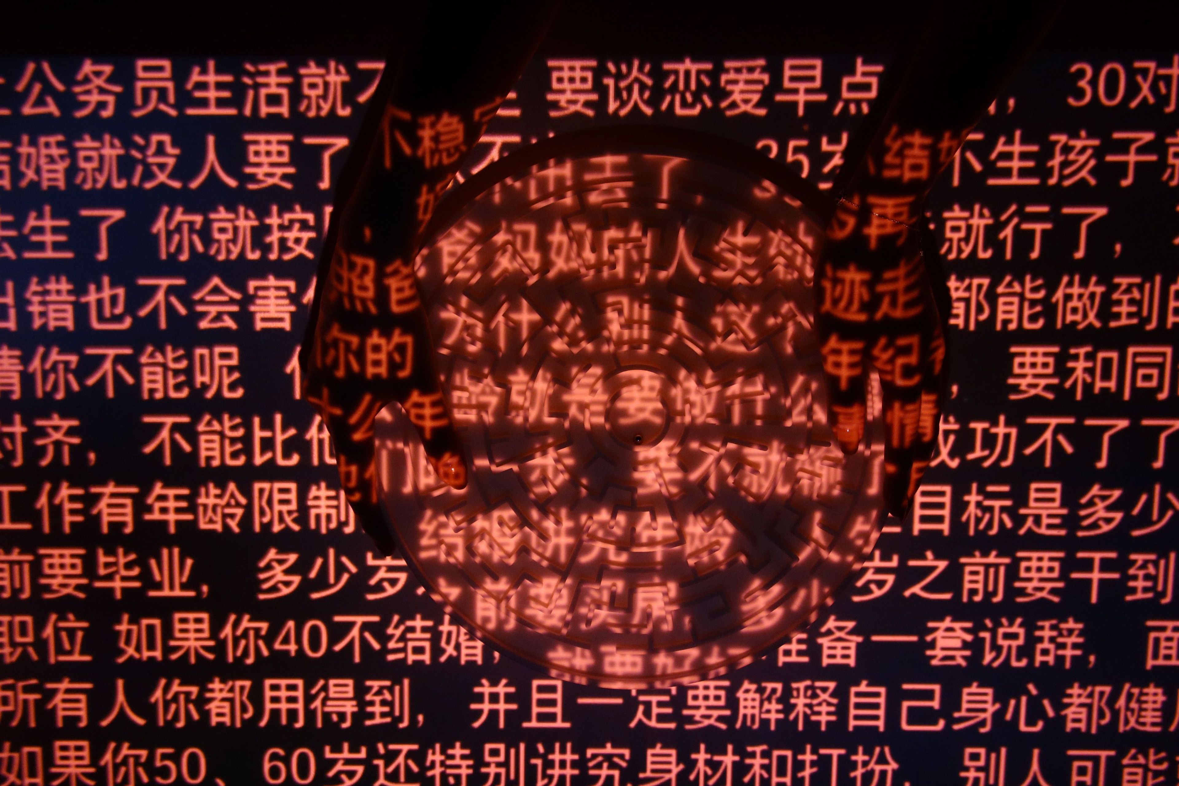 Photograph of hands holding a wheel in darkness, with rows of red Chinese characters projected onto them.