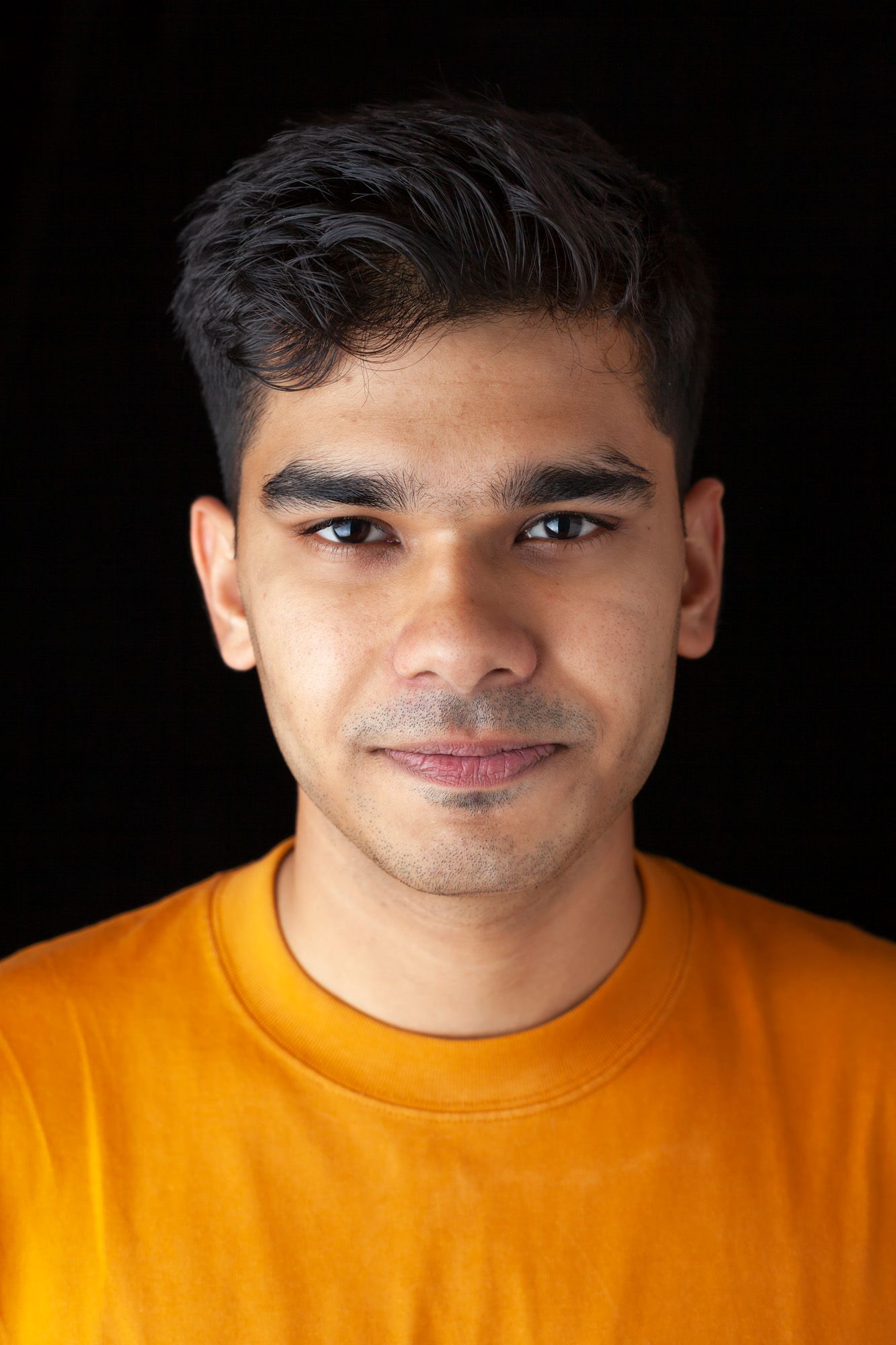 Portrait of a man wearing a mustard-yellow shirt against a black background