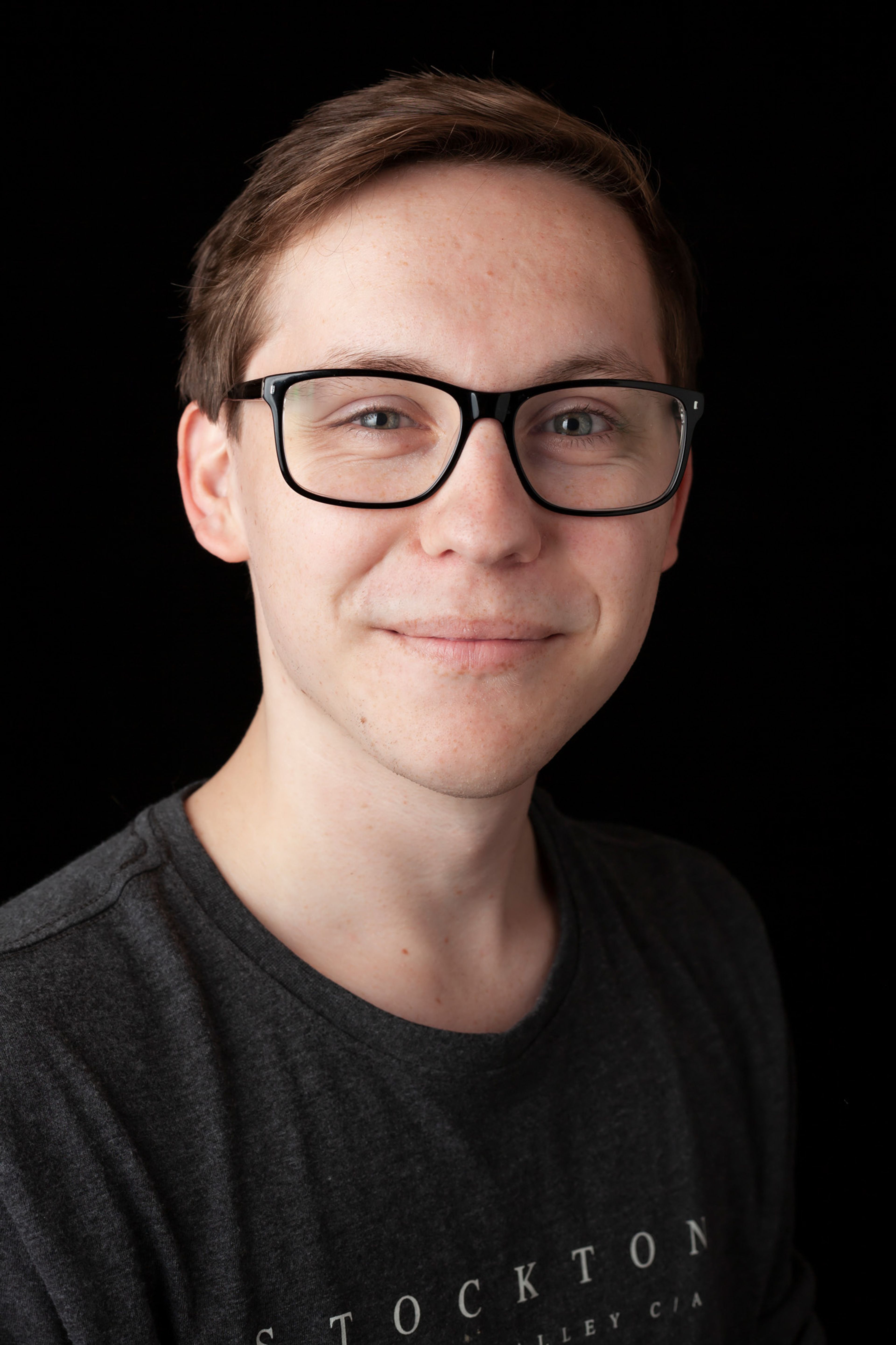 A portrait of a young man wearing glasses and a dark grey t-shirt