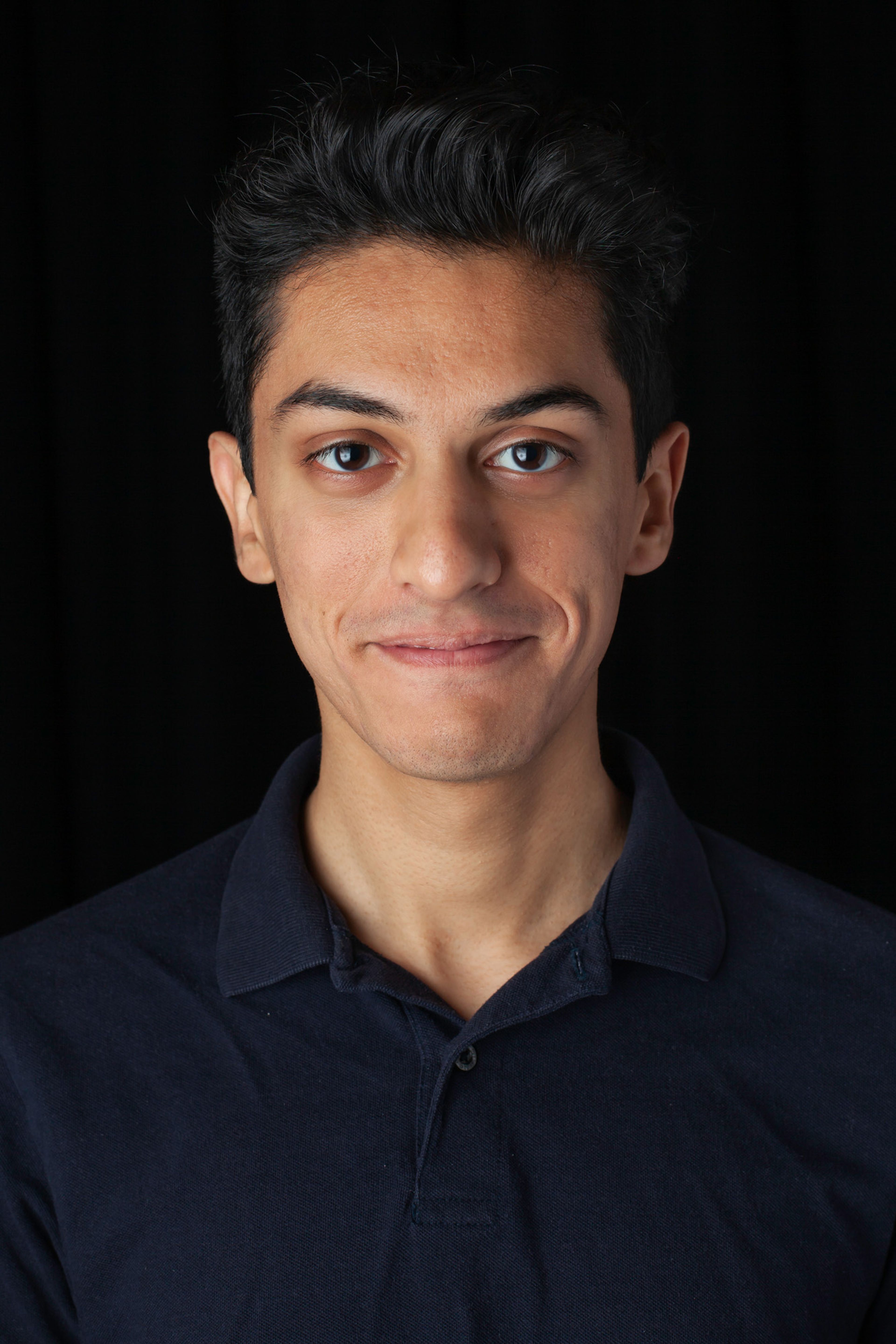 An individual with short, dark hair and a clean-shaven face, wearing a navy blue collared shirt