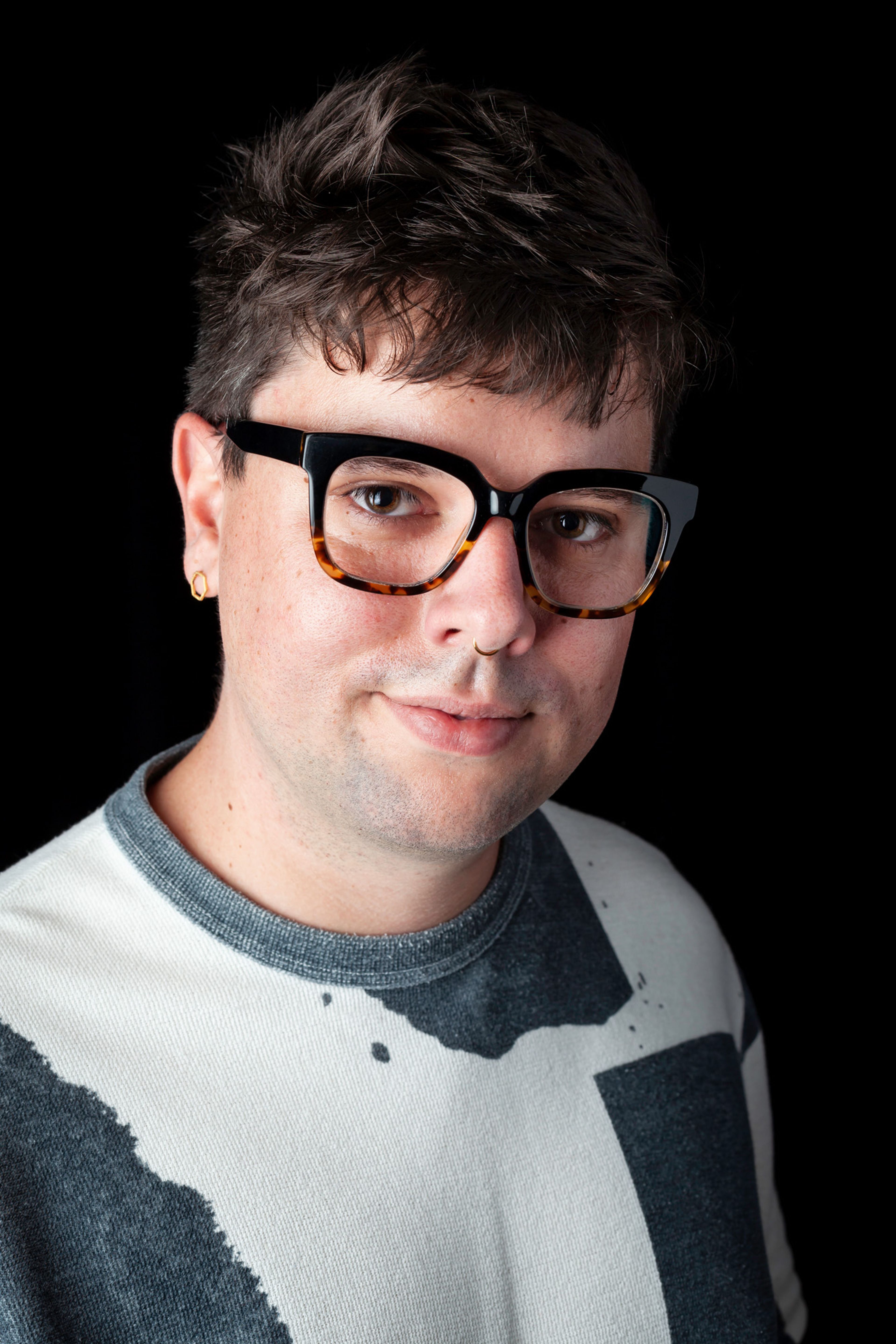 Portrait of a person with short, textured hair and glasses with bold, black-and-tortoiseshell frames