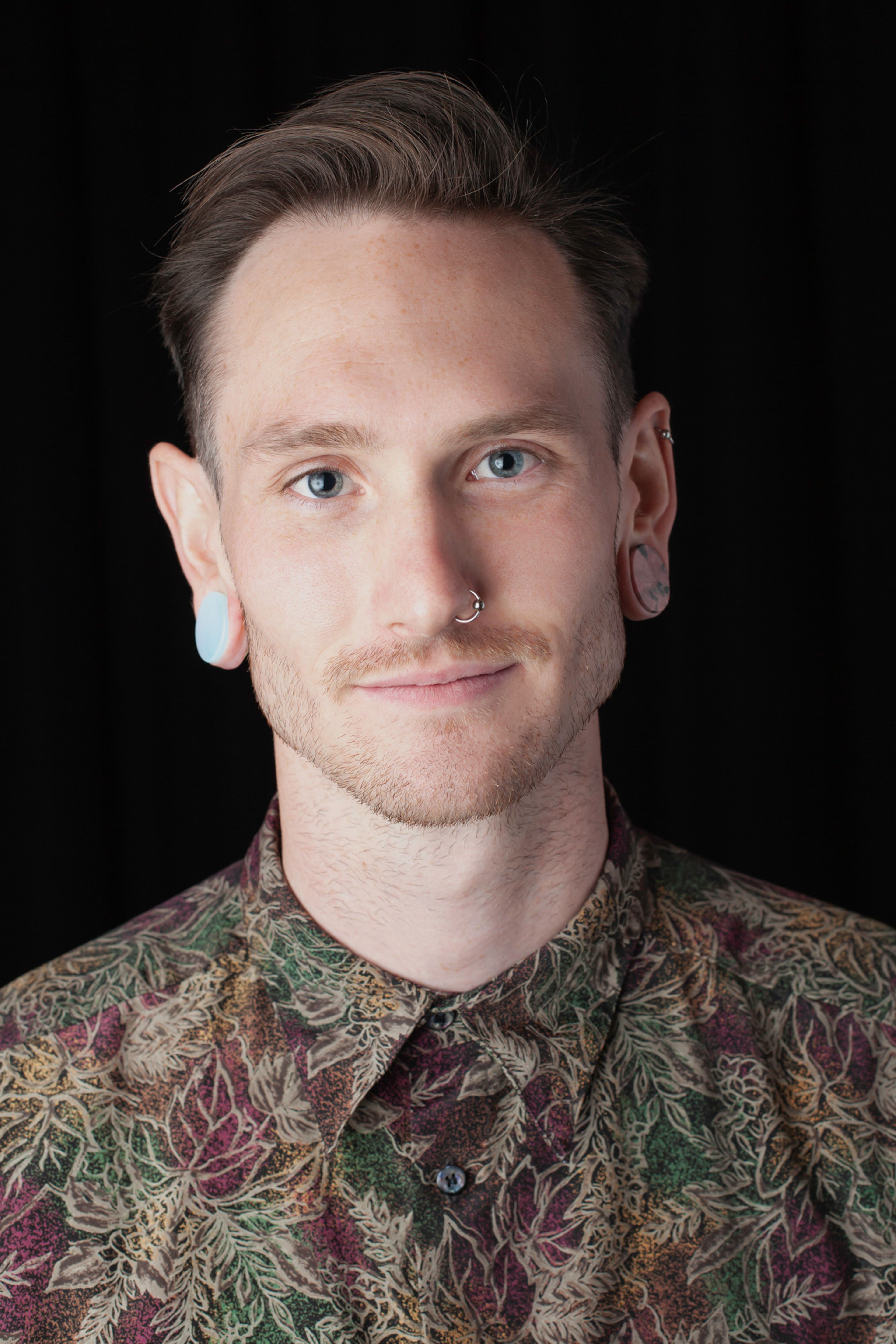 A portrait of a person with light hair styled neatly, wearing a patterned shirt with earthy tones