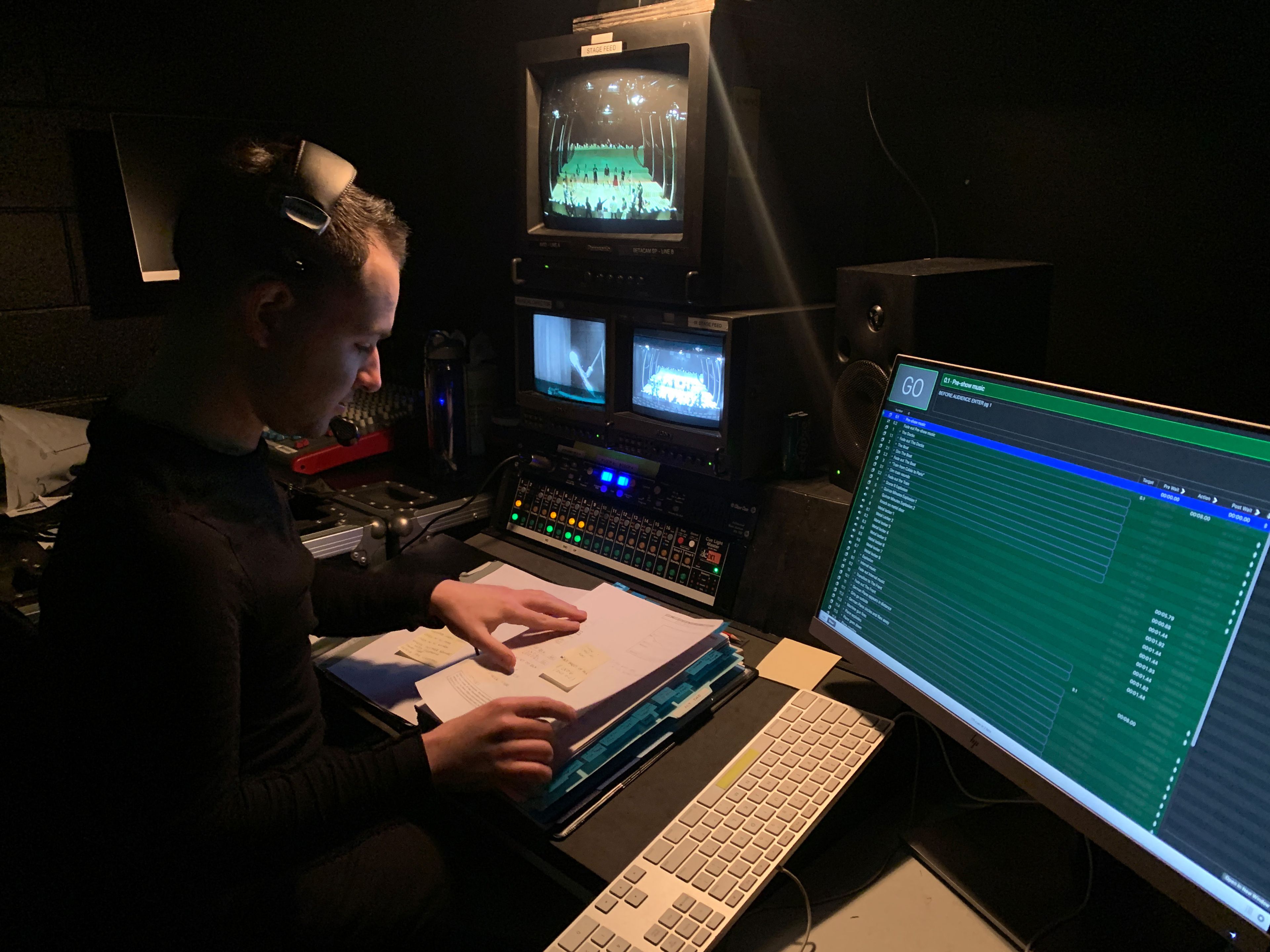 An individual working in a control room wearing a headset and black attire, they are focused on a script