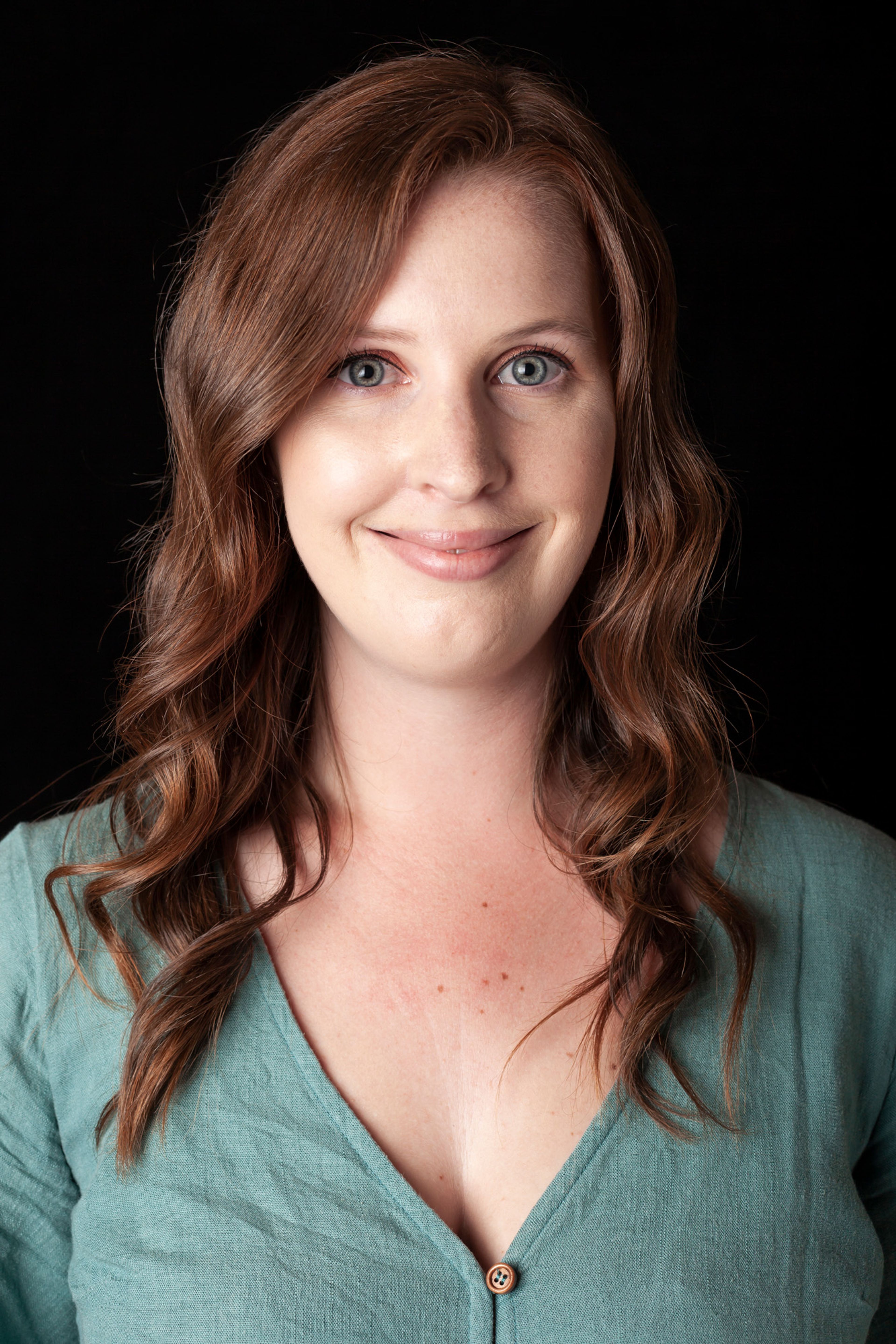 A portrait of a woman with long, wavy auburn hair, wearing a teal blouse with a button detail