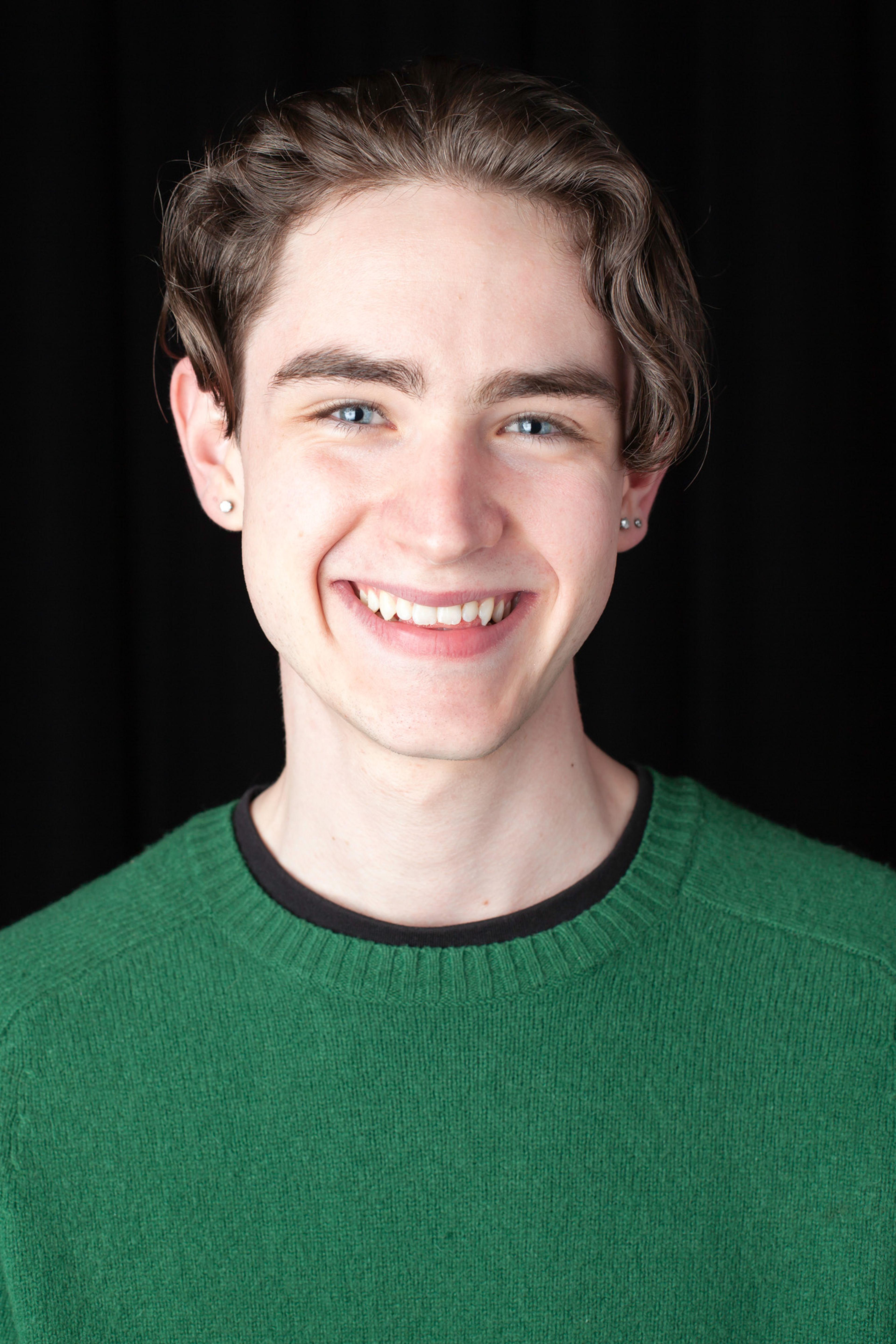 A portrait of a smiling individual wearing a green sweater and black undershirt