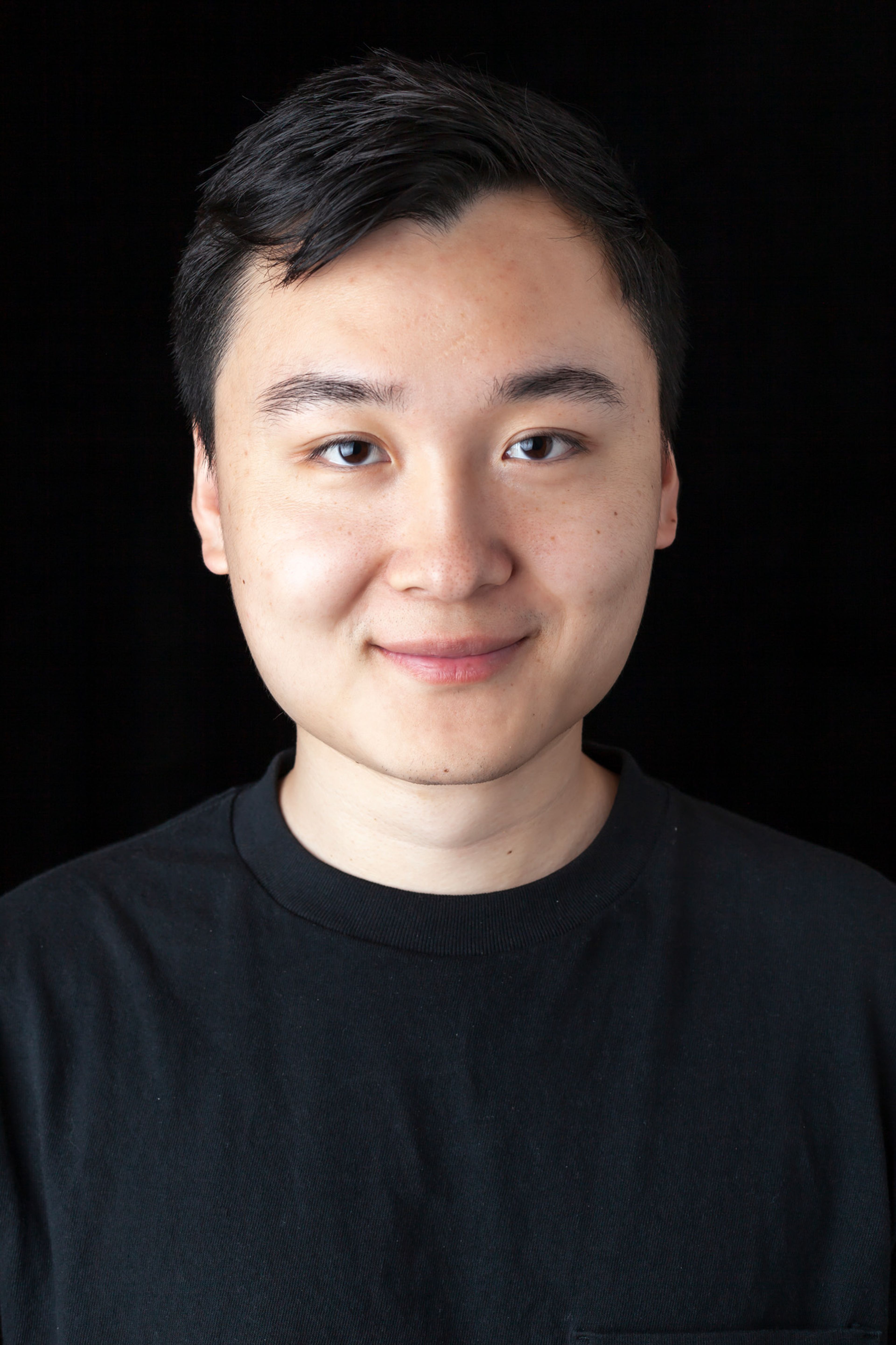 Portrait of a person with short, dark hair, wearing a black t-shirt, smiling slightly