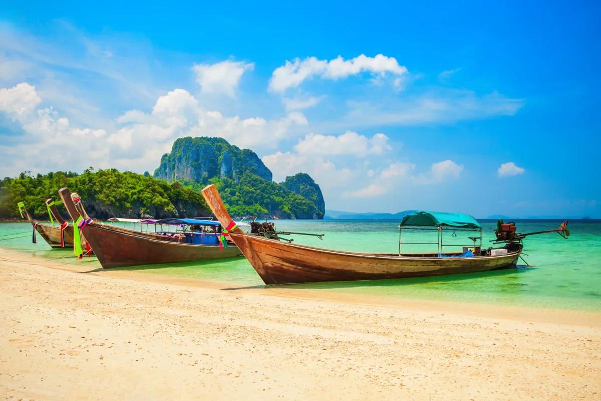 Longtail boats beached on white sand below a limestone island in the Gulf of Thailand