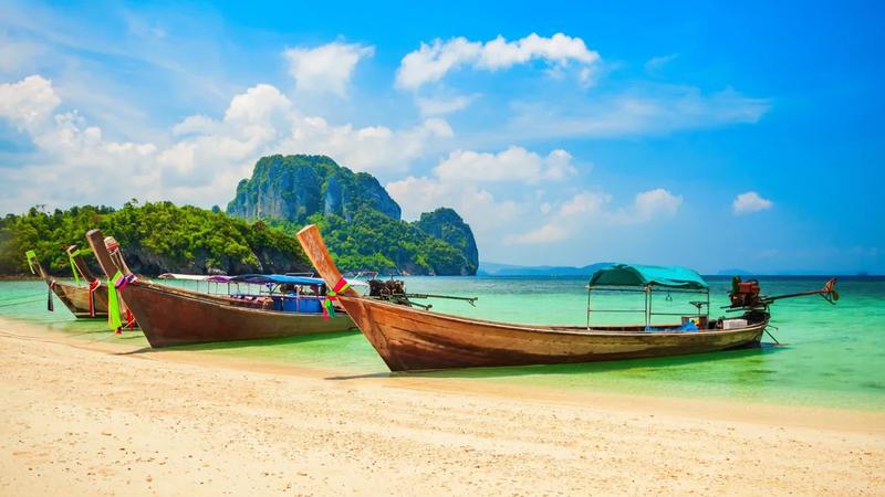 Longtail boats beached on white sand below a limestone island in the Gulf of Thailand