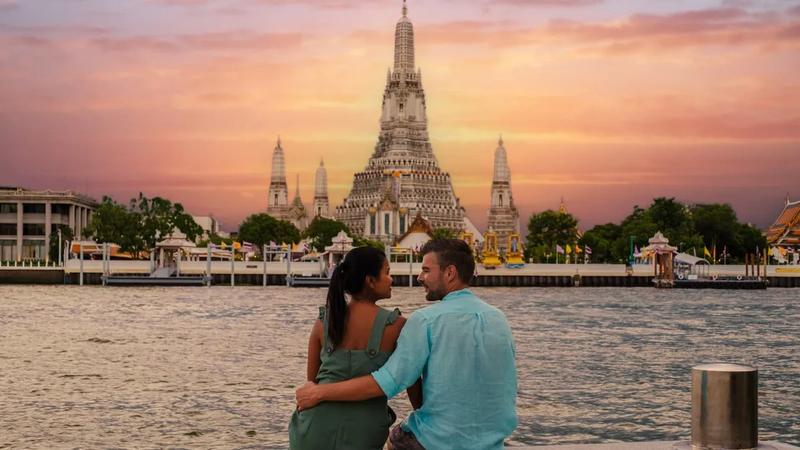 A couple watching the sunset behind Wat Arun across the Chao Phraya river in Bangkok