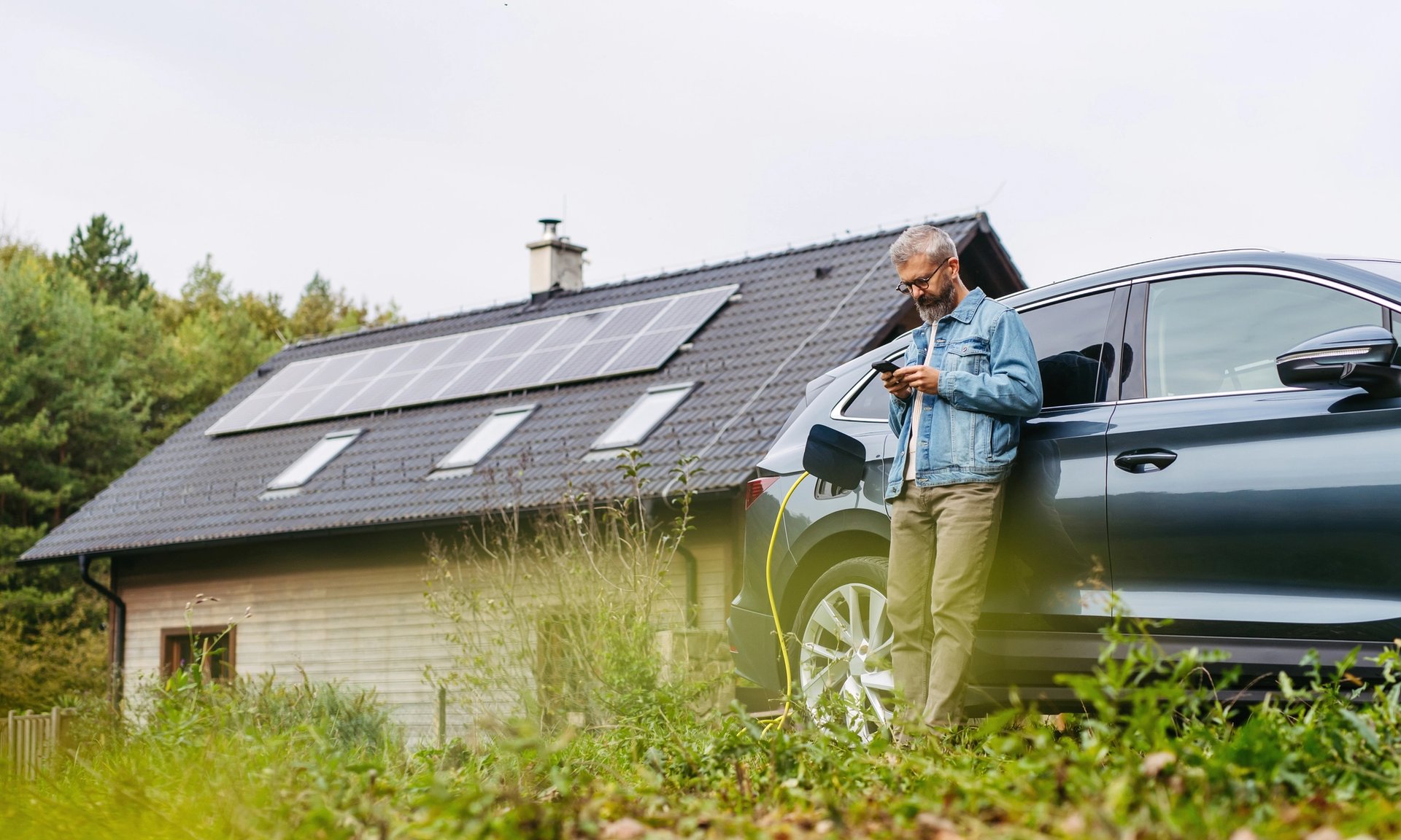 Ein Mann lädt sein Elektroauto vor seinem Haus mit Solar auf dem Dach.
