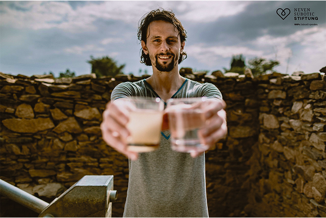 Ein Mann, Neven Subotic, hält mit ausgestreckten Armen zwei Gläser Wasser nach vorne. 