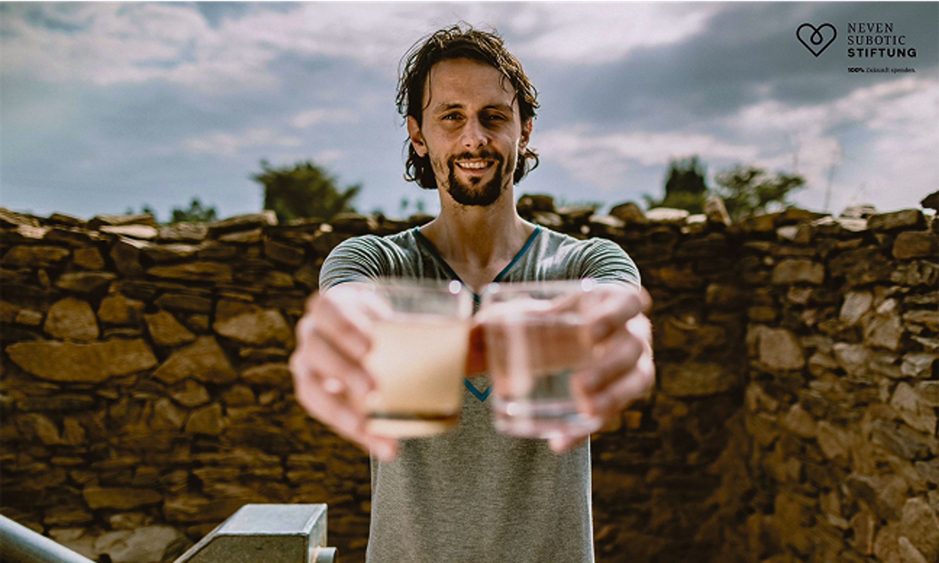 A man, Neven Subotic, holds two glasses of water out in front of him with his arms outstretched.