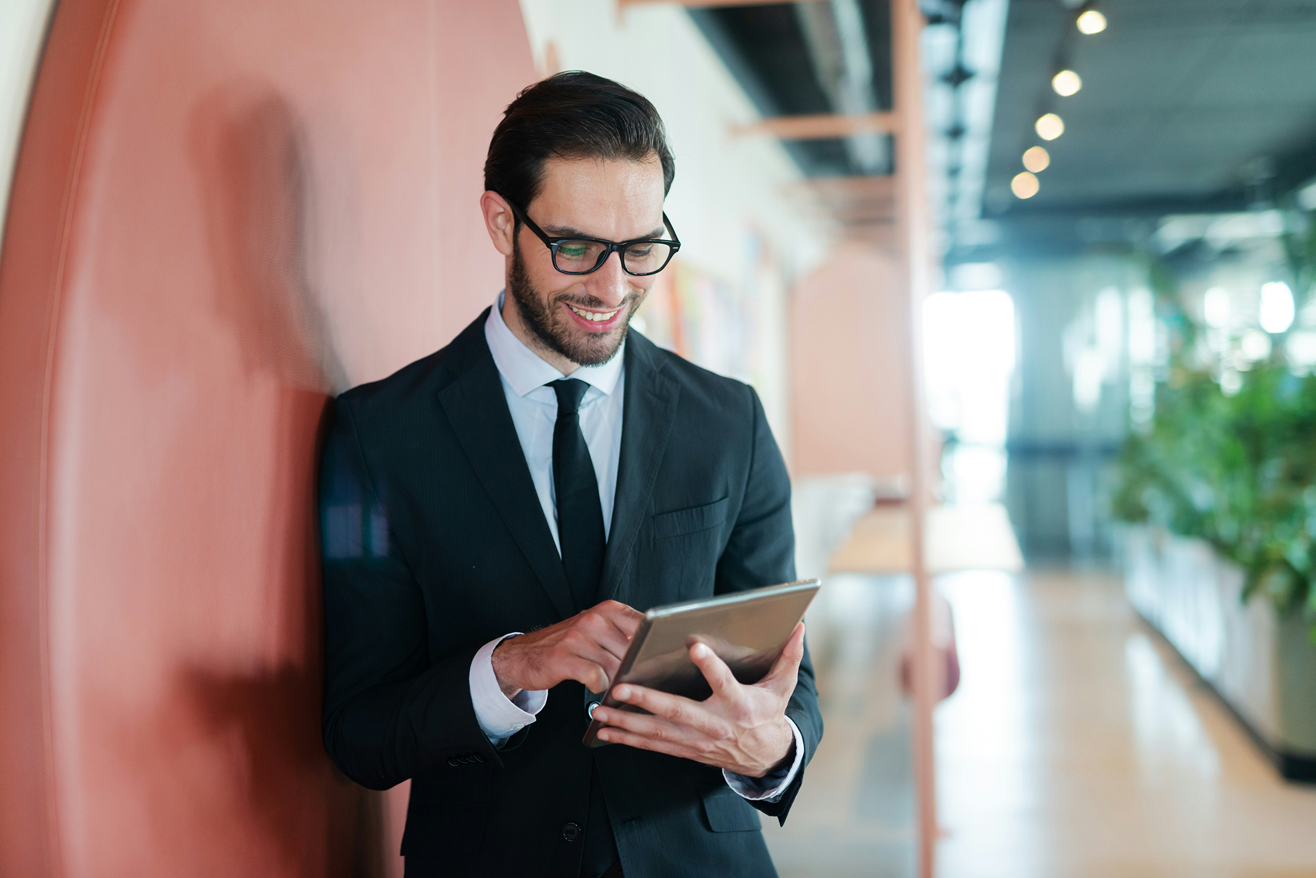 Man in a suit leaning against a red wall, looking at a tablet with Data Cloud in his hands.