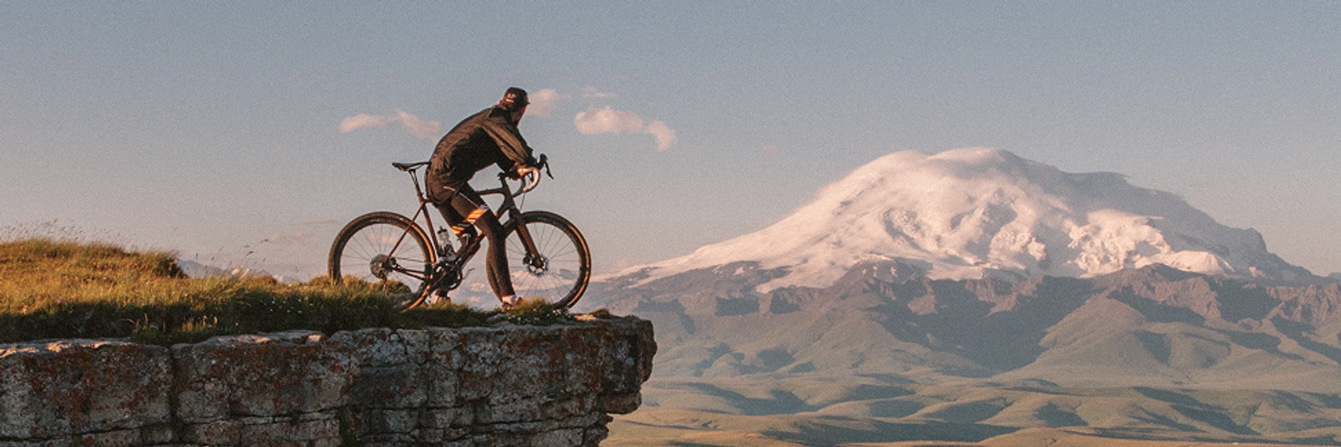 Ein Fahrradfahrer steht an einer Felskante, im Hintergrund ein schneebedeckter Berg.