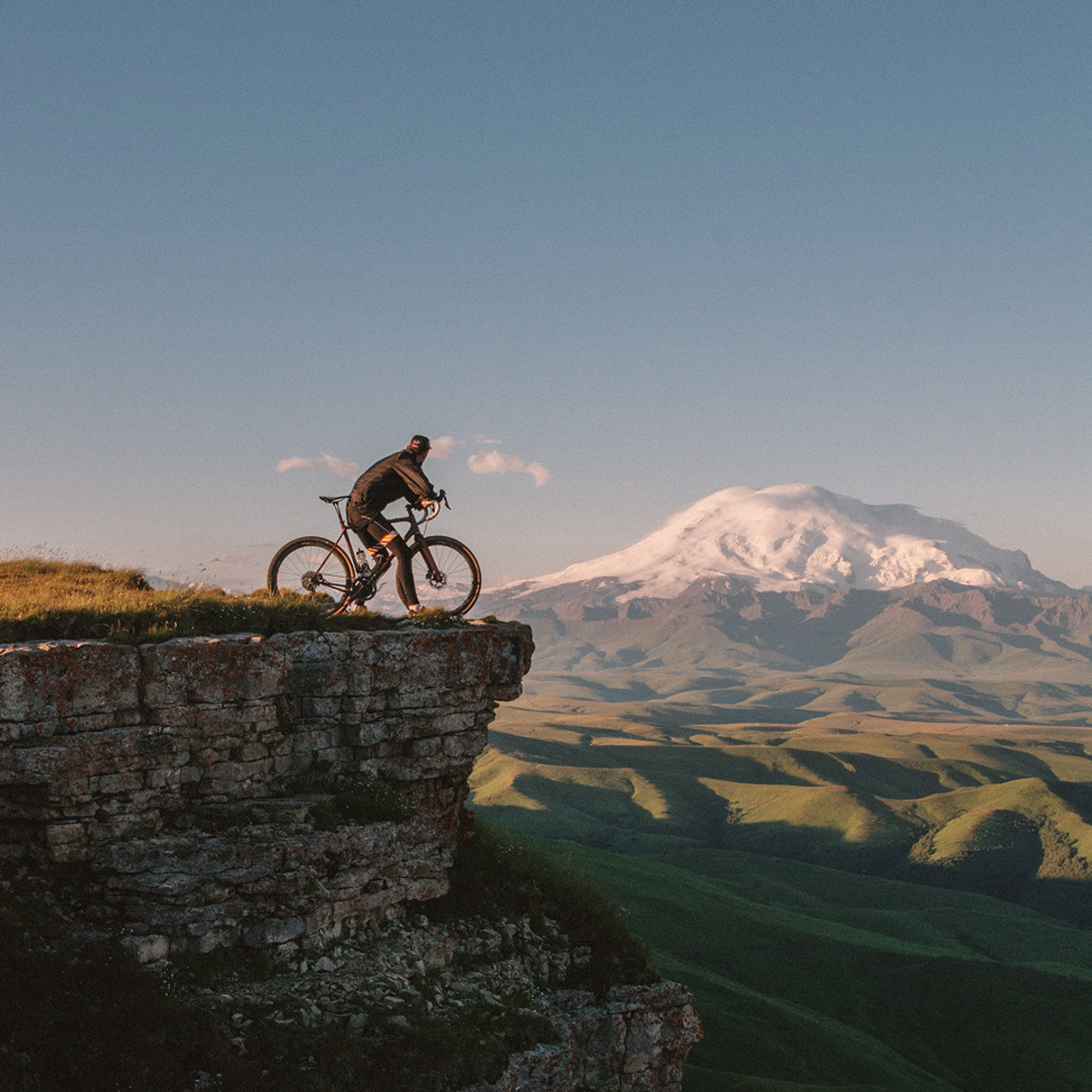 Ein Fahrradfahrer steht an einer Felskante, im Hintergrund ein schneebedeckter Berg.