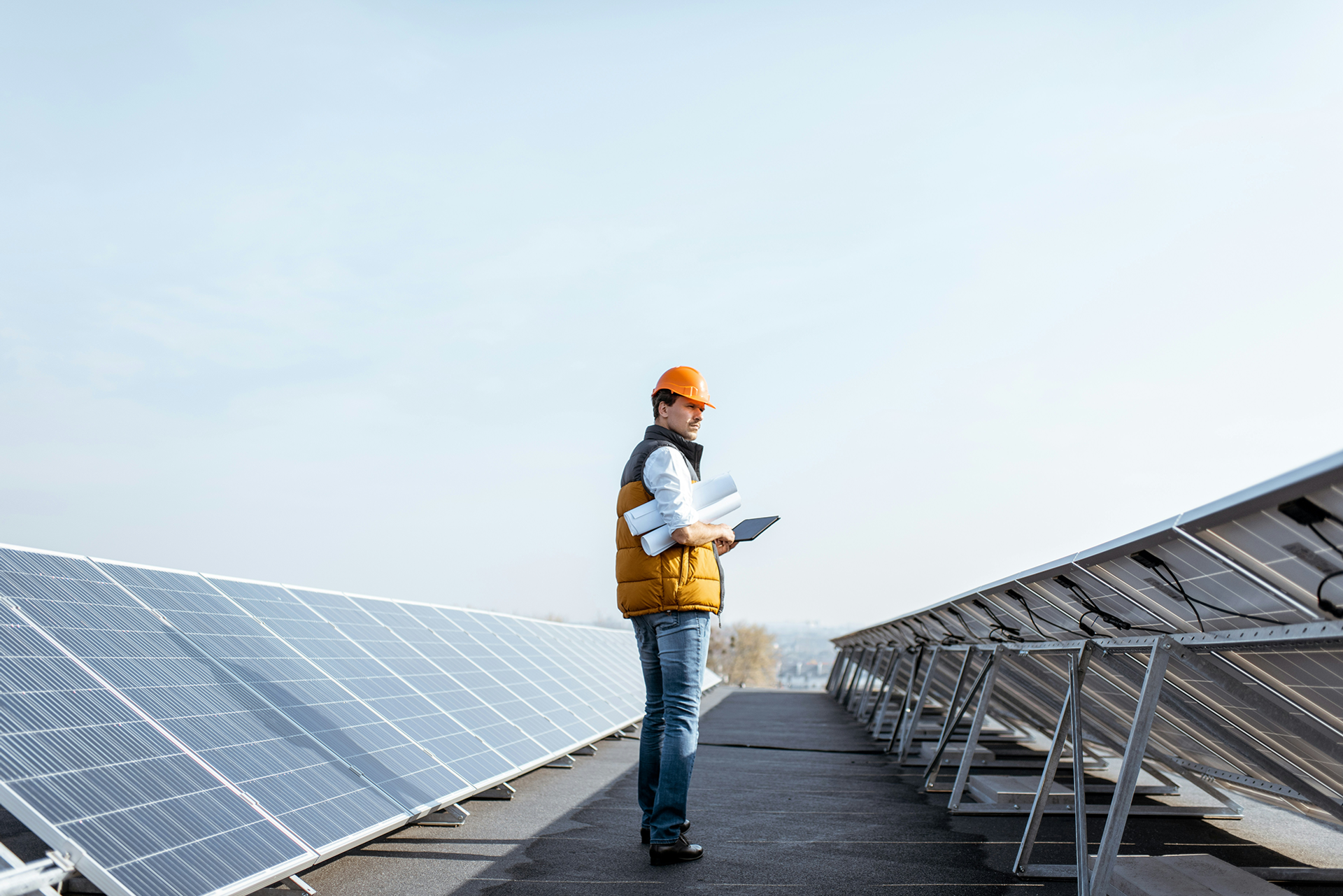 Ingenieur steht mit Tablet und Salesforce Energy & Utilities Cloud und aufgerollten Plänen zwischen Solarpanelen.
