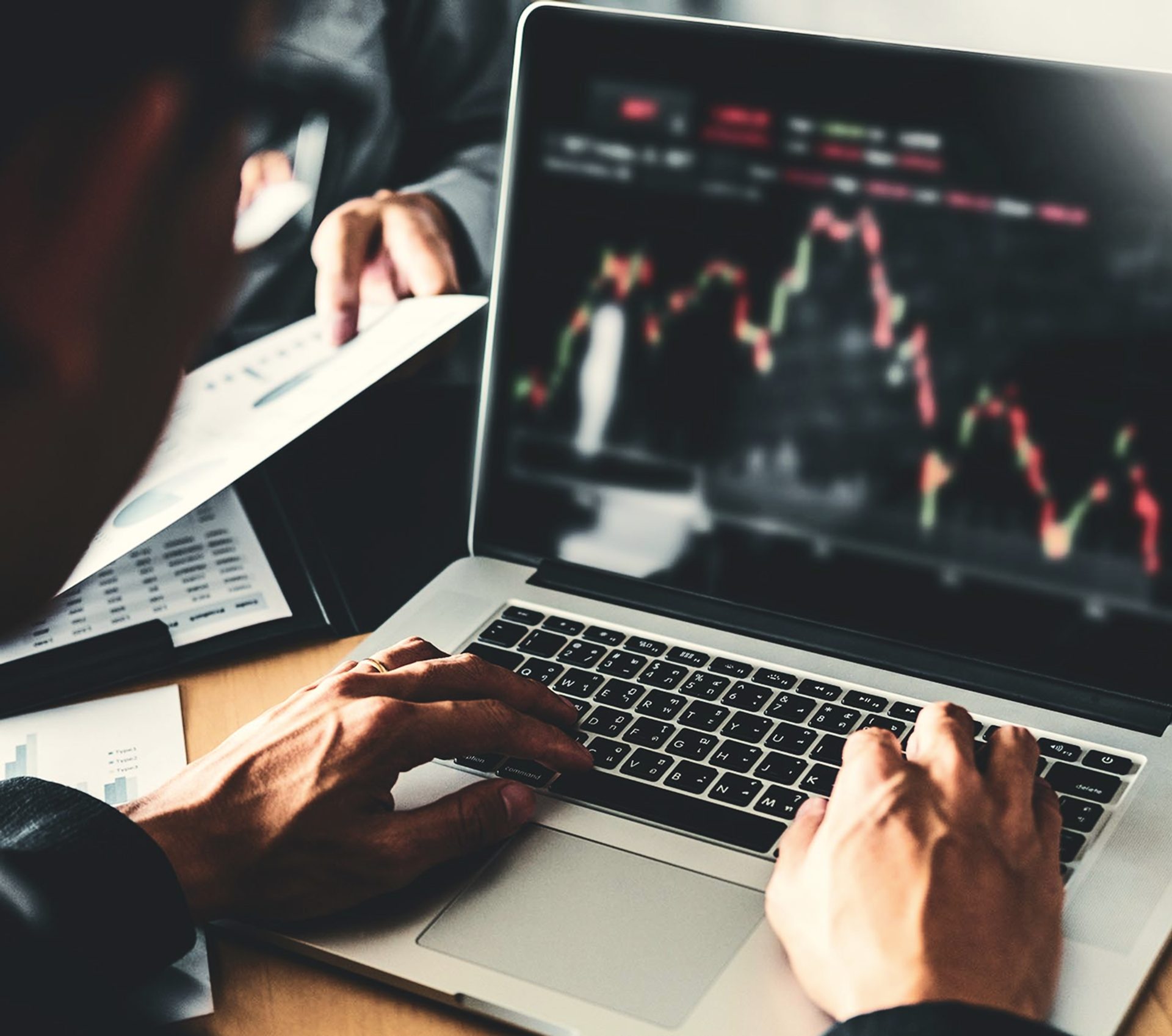 Blick über die Schulter eines Mannes auf einen Laptop, seine Hände auf der Tastatur.