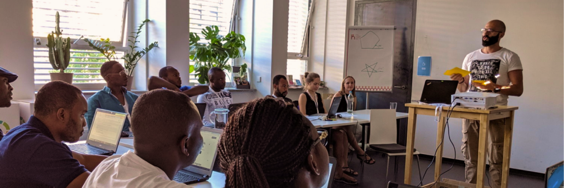 Ein Lehrer der ReDI School steht vor einer erwachsenen Klasse und unterrichtet.
