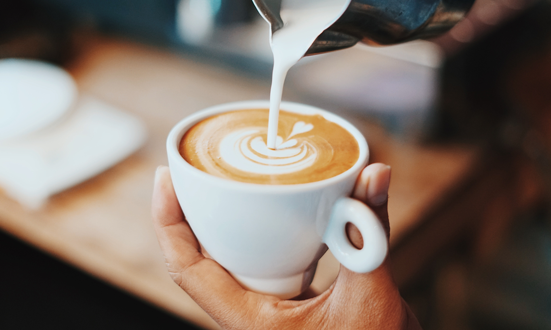 Milch wird in einen Cappuccino gegossen.