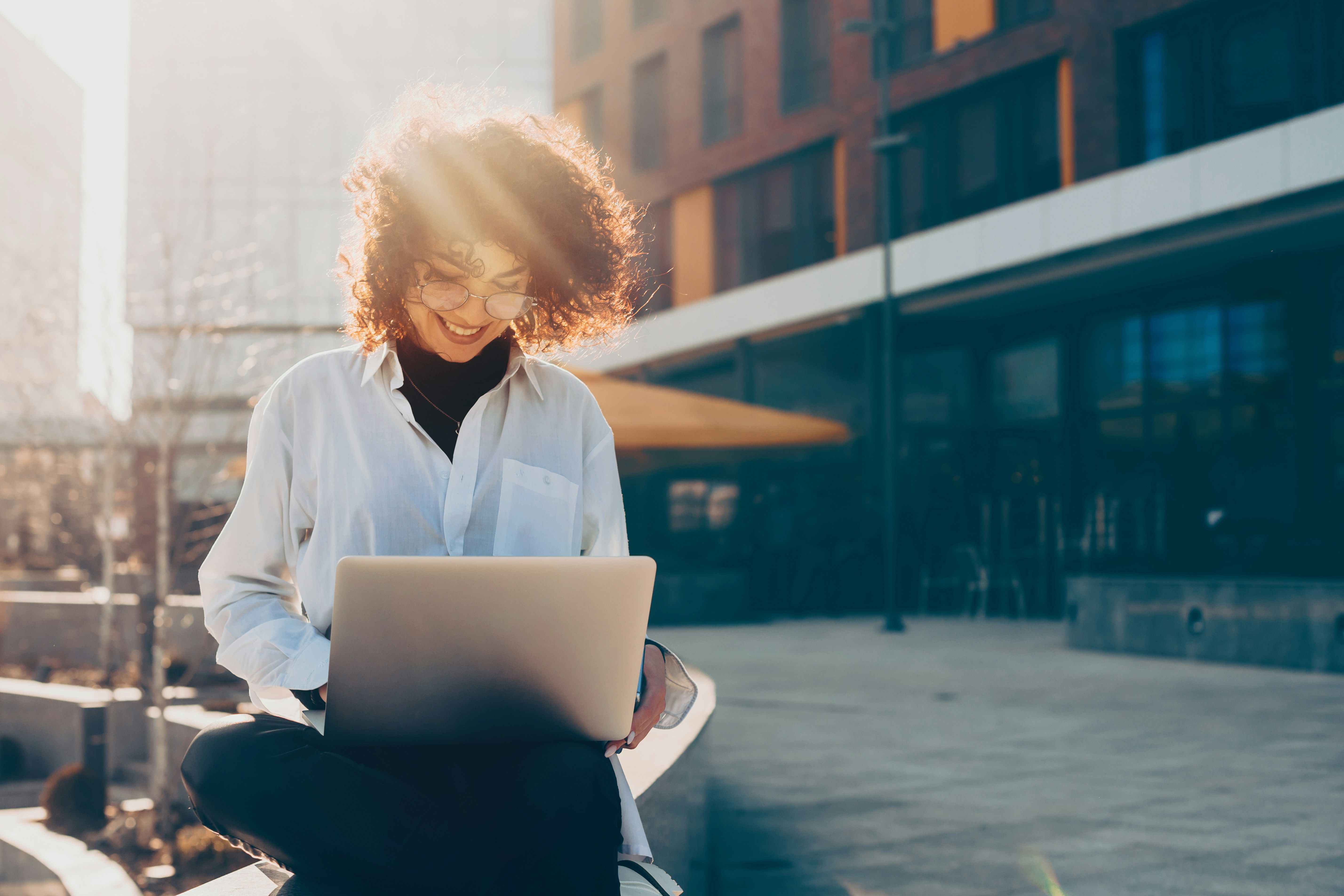 A woman sits outdoors and works on a laptop.