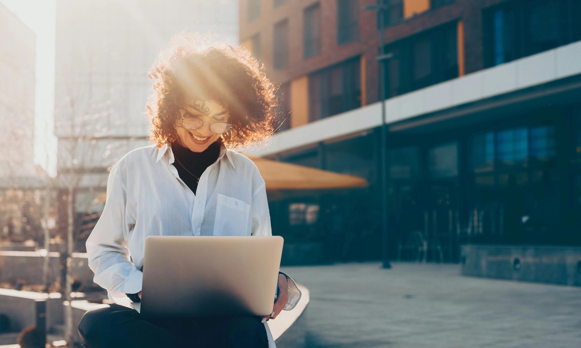 A woman sits outdoors and works on a laptop.