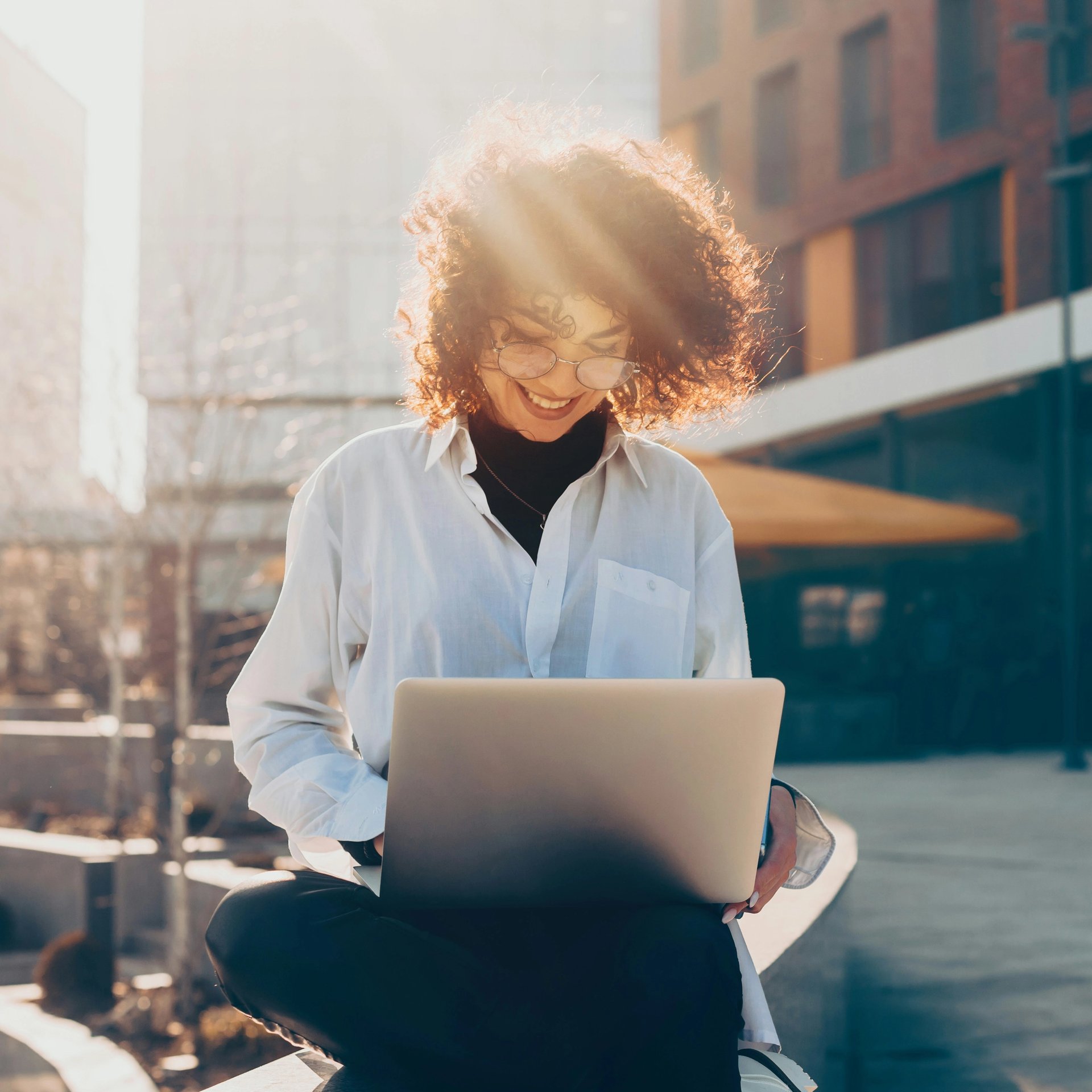 A woman sits outdoors and works on a laptop.