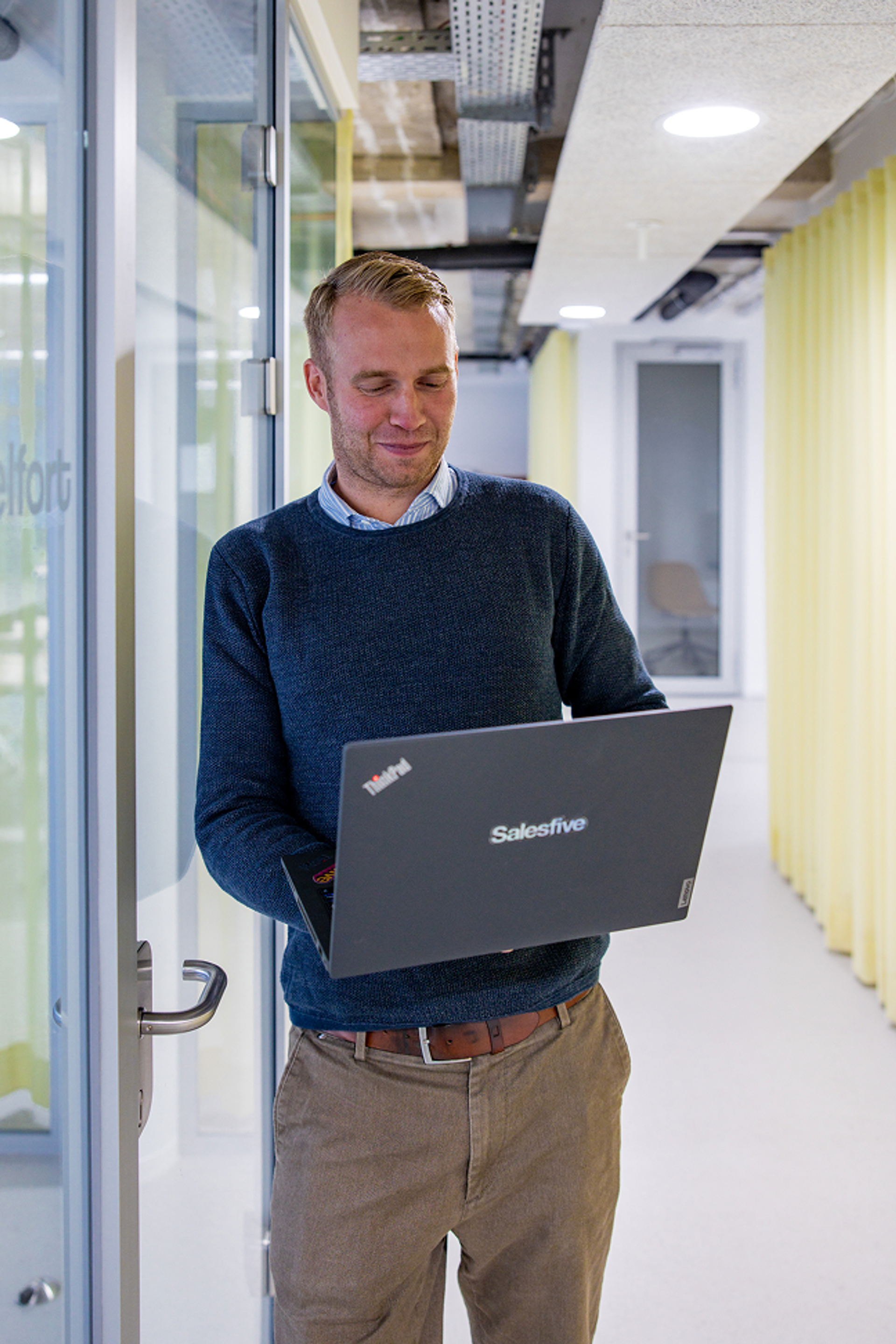Salesfive Kollege steht mit Laptop im Flur. 