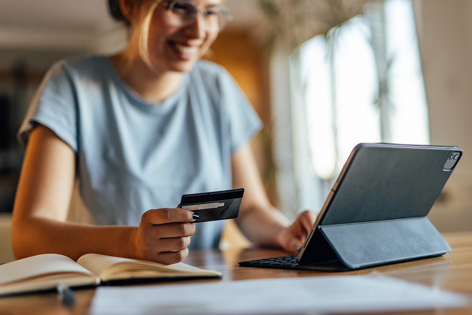 A woman sits in front of a tablet with a credit card in her hand.