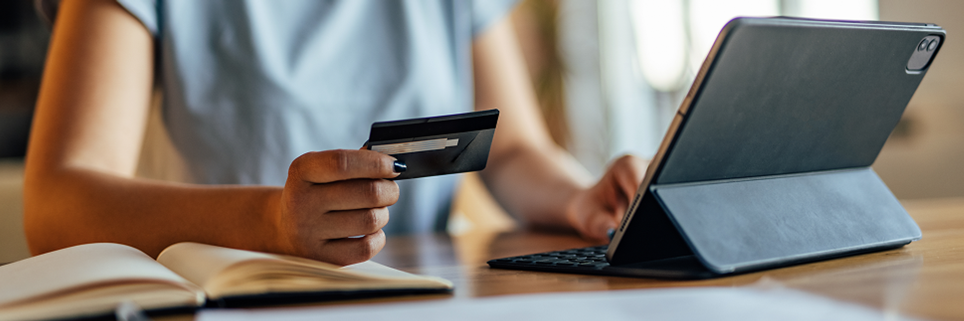 A woman sits in front of a tablet with a credit card in her hand.