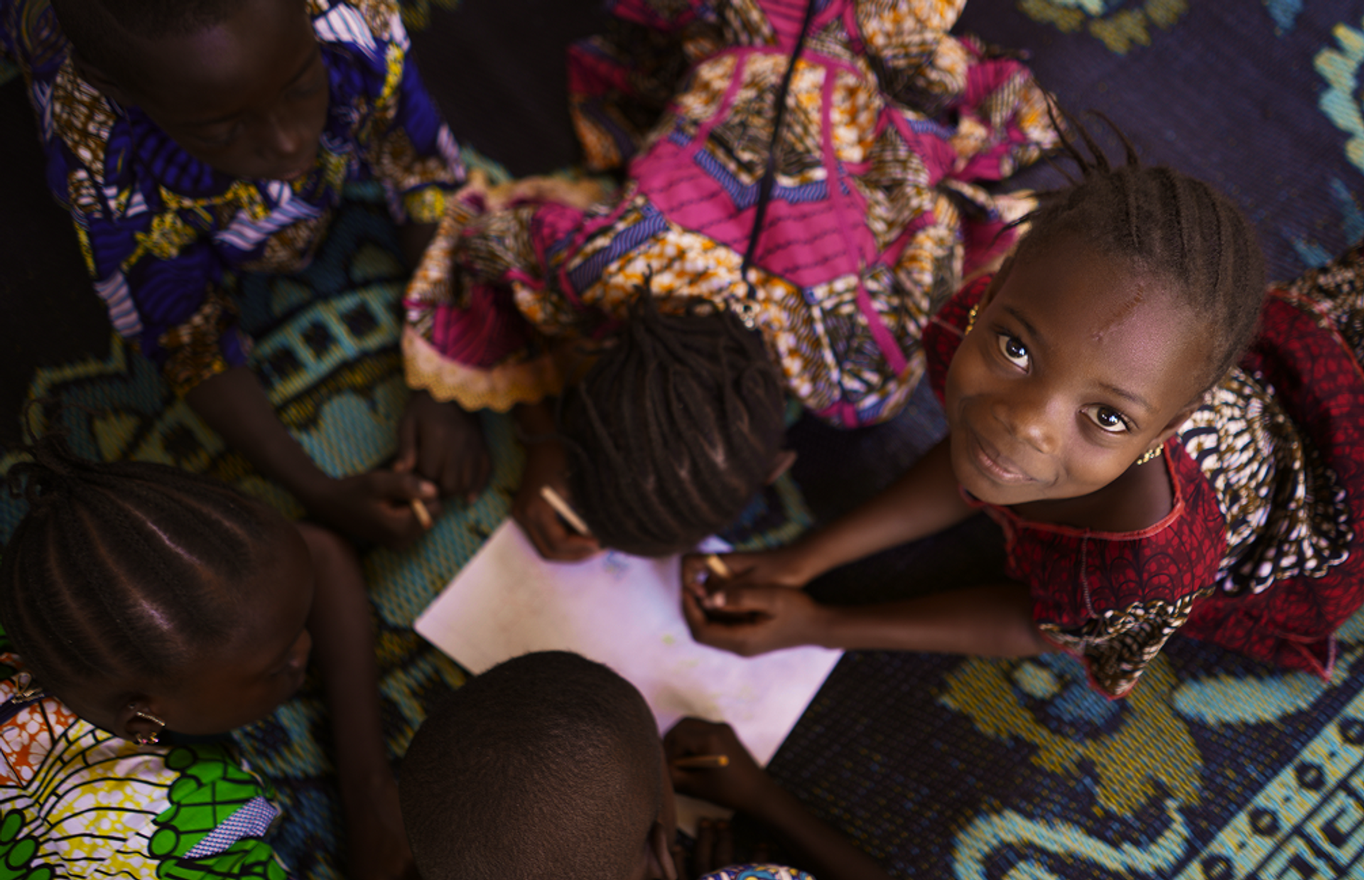 Ein Mädchen sitzt auf dem Boden und schaut nach oben in dir Kamera.