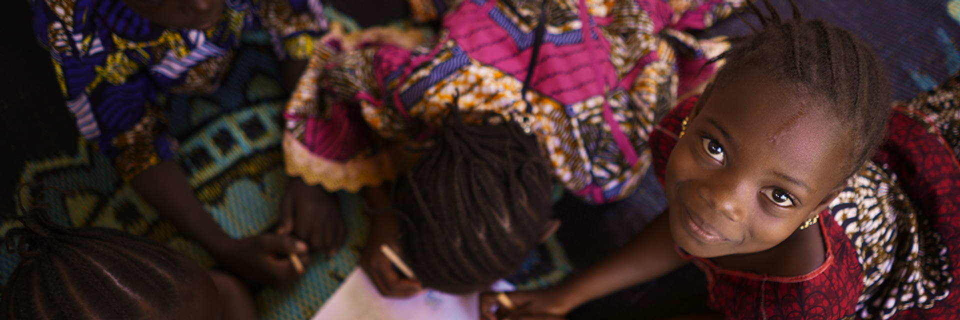 Ein Mädchen sitzt auf dem Boden und schaut nach oben in dir Kamera.