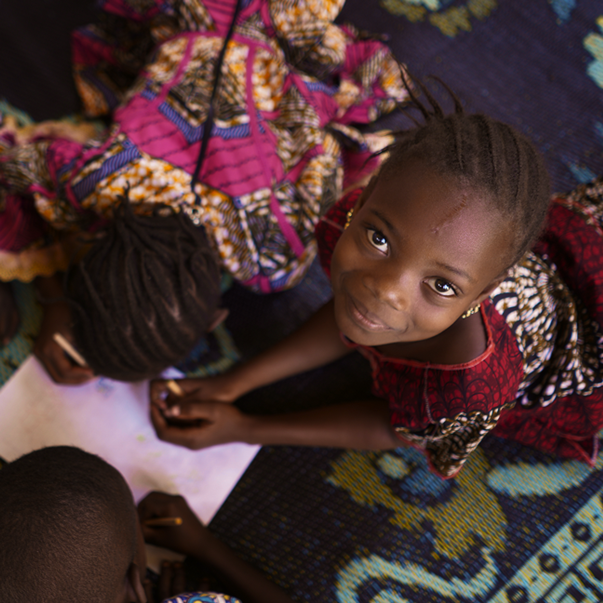Ein Mädchen sitzt auf dem Boden und schaut nach oben in dir Kamera.