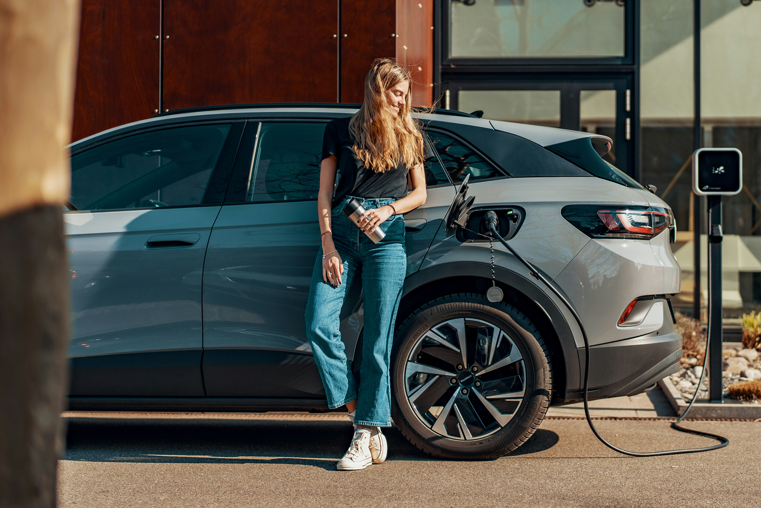 Frau lehnt sich an E-Auto beim Laden.