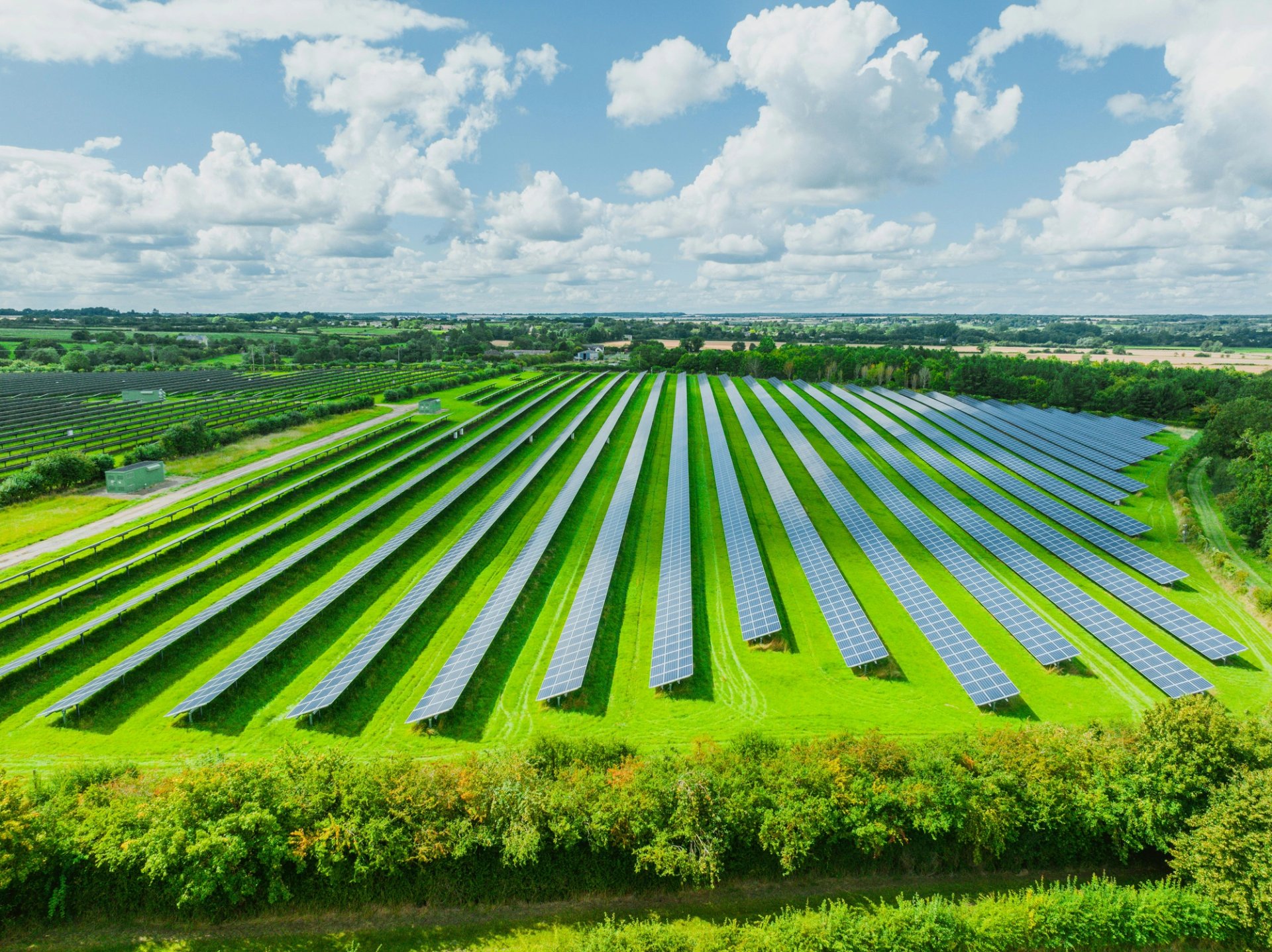 A solar park in a green field beneath a blue sky.