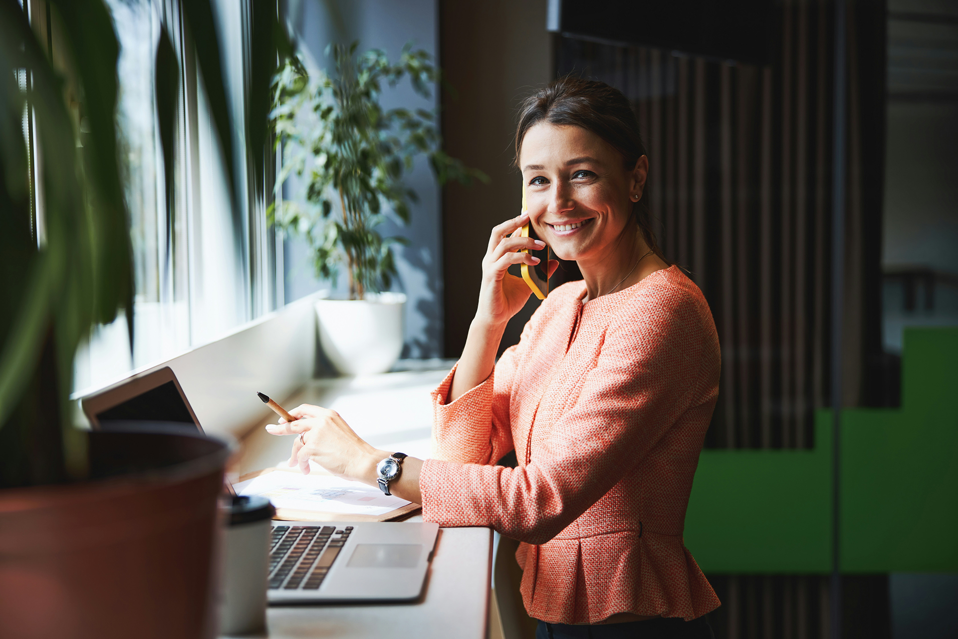 Frau mit rosa Oberteil telefoniert, neben sich Laptop mit Salesforce Nonprofit Cloud, und lächelt in die Kamera.