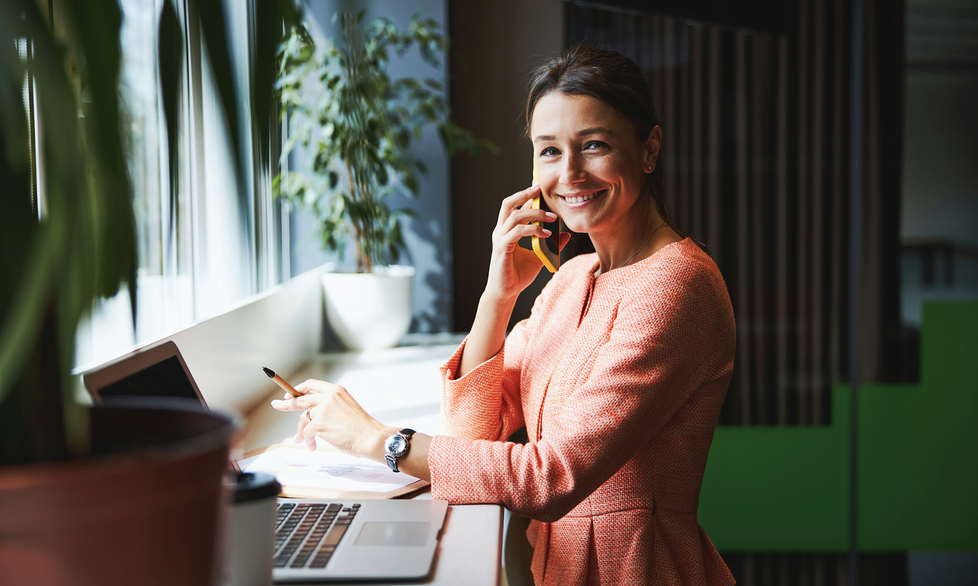 Woman wearing a pink top is on the phone, with a laptop running Salesforce Agentforce Nonprofit next to her, smiling at the camera.