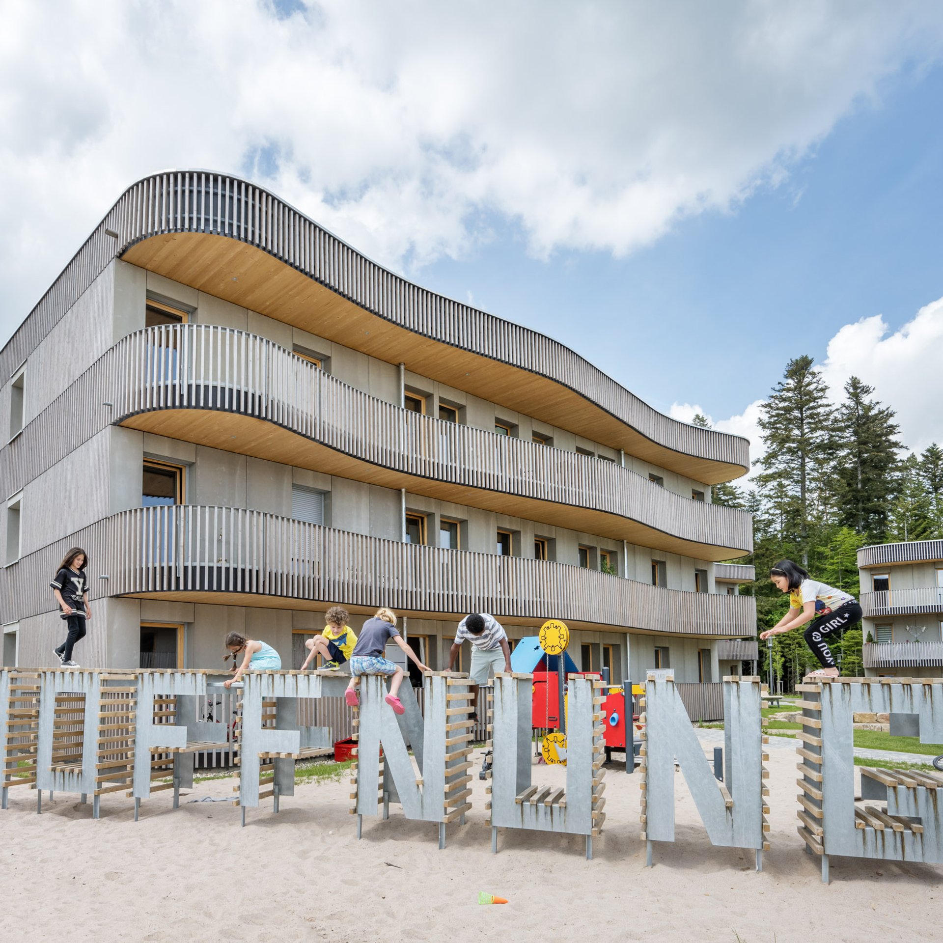Kinder spielen auf einem Hoffnung-Schriftzug vor einem Holzhaus.