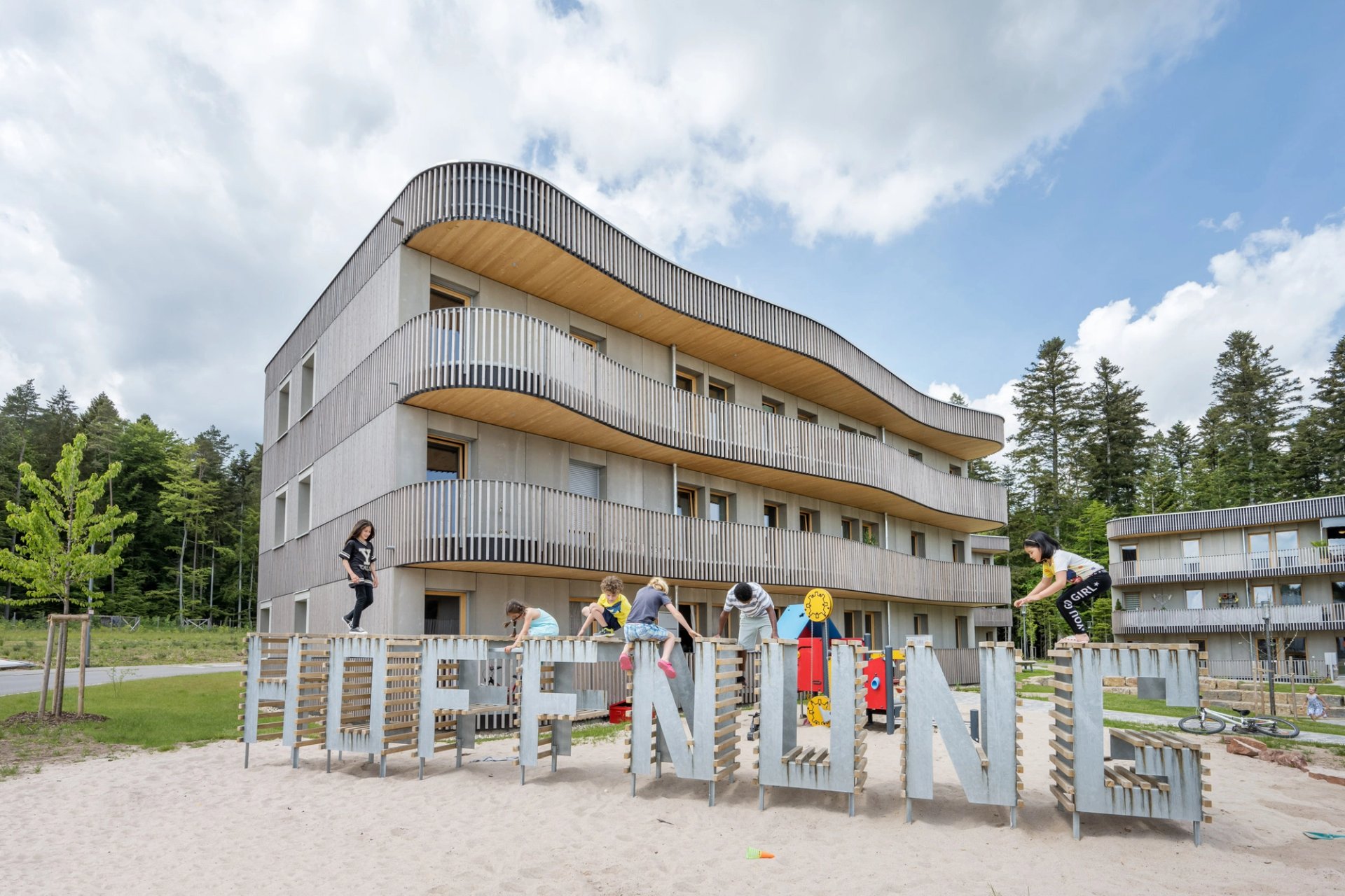 Kinder spielen auf einem Hoffnung-Schriftzug vor einem Holzhaus.