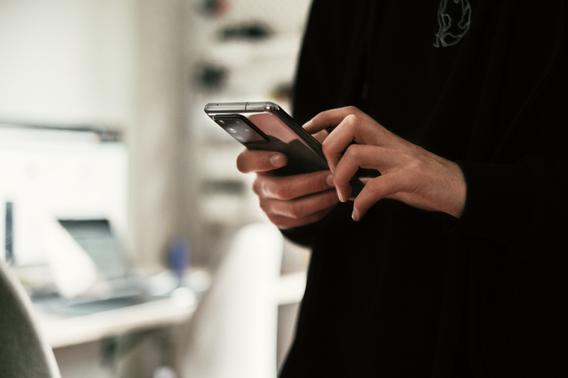 Person mit schwarzem Pullover hält ein Smartphone vor sich.