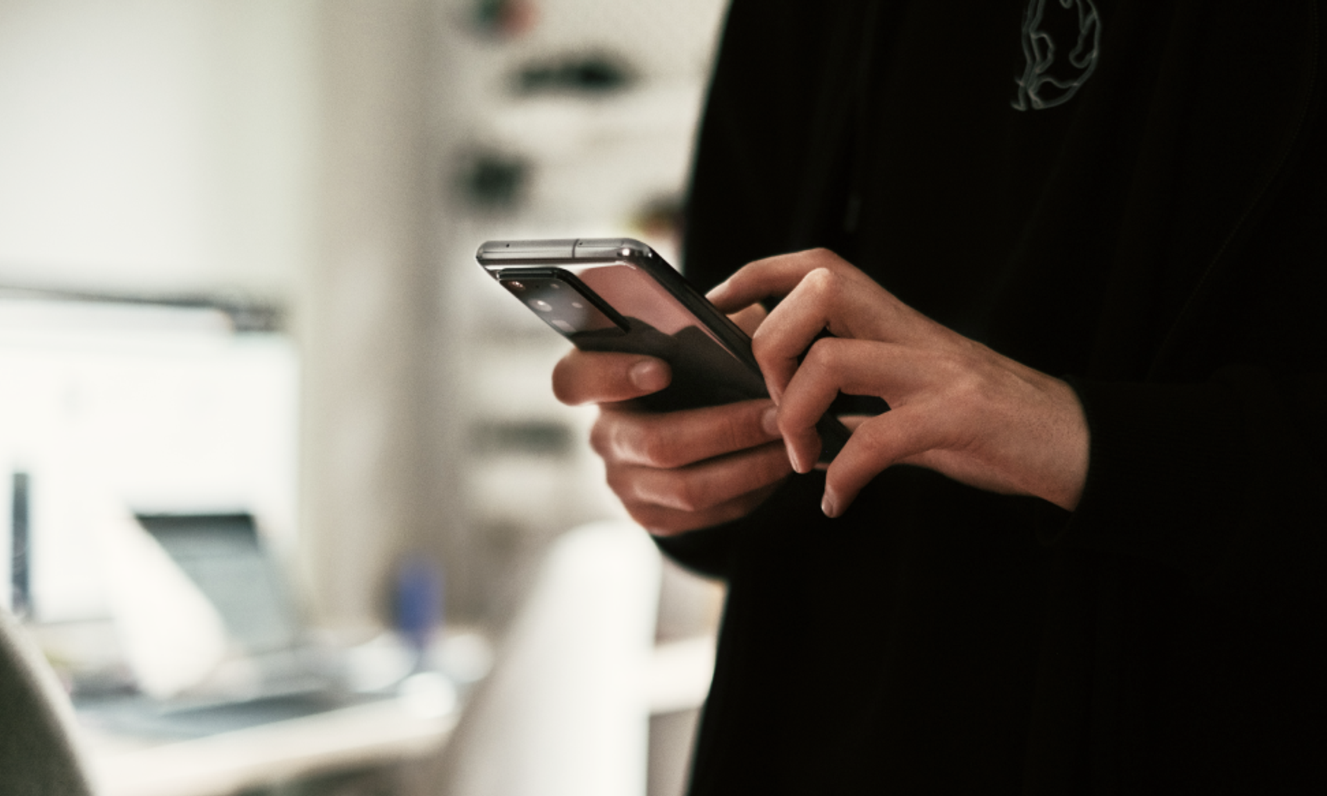 Person mit schwarzem Pullover hält ein Smartphone vor sich.