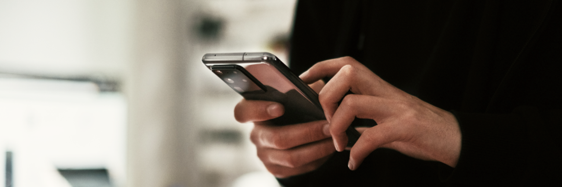 Person mit schwarzem Pullover hält ein Smartphone vor sich.