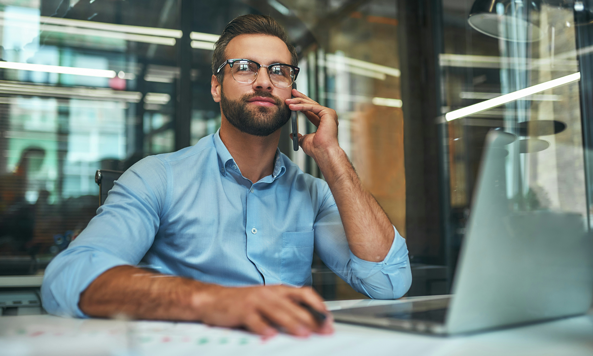 Man sitting at a desk in front of a laptop with Agentforce Service, talking on his cell phone.