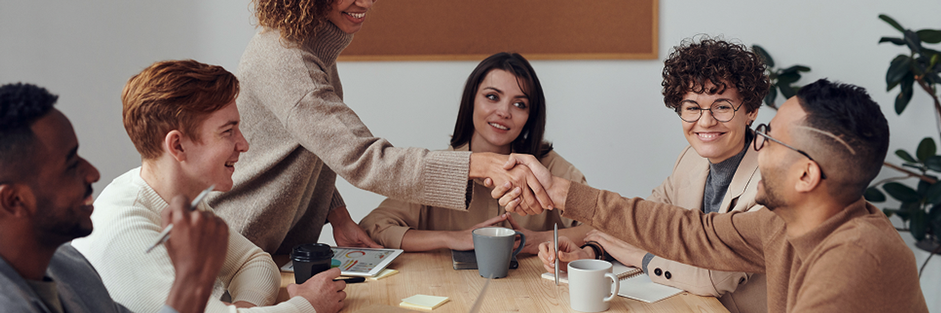 Sechs Menschen sitzen am Tisch, zwei reichen sich die Hand.