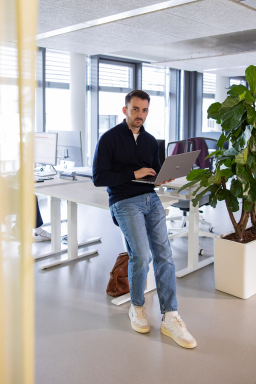 Salesfive Kollege steht mit Laptop in Office in Düsseldorf.