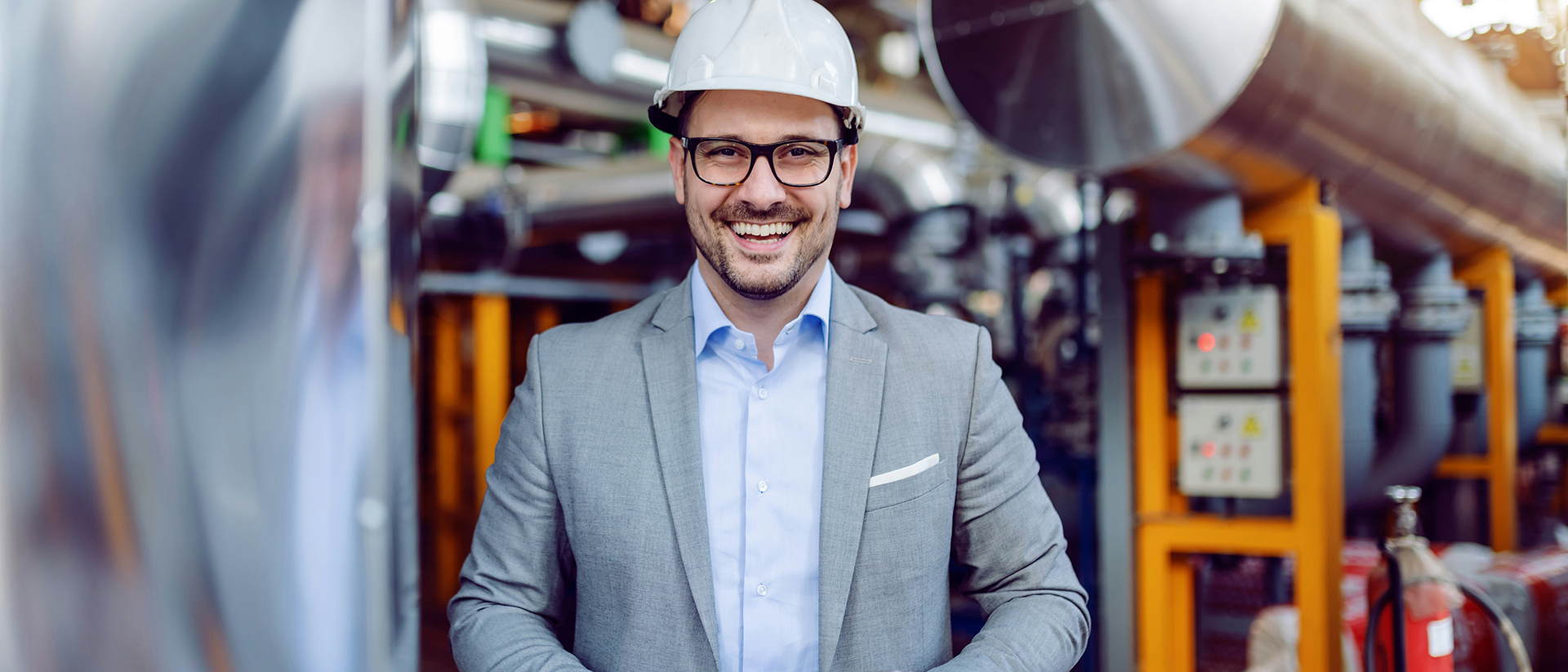 Mann mit Helm und Tablet mit Manufacturing Cloud steht in Fertigungshalle und schaut in Kamera.