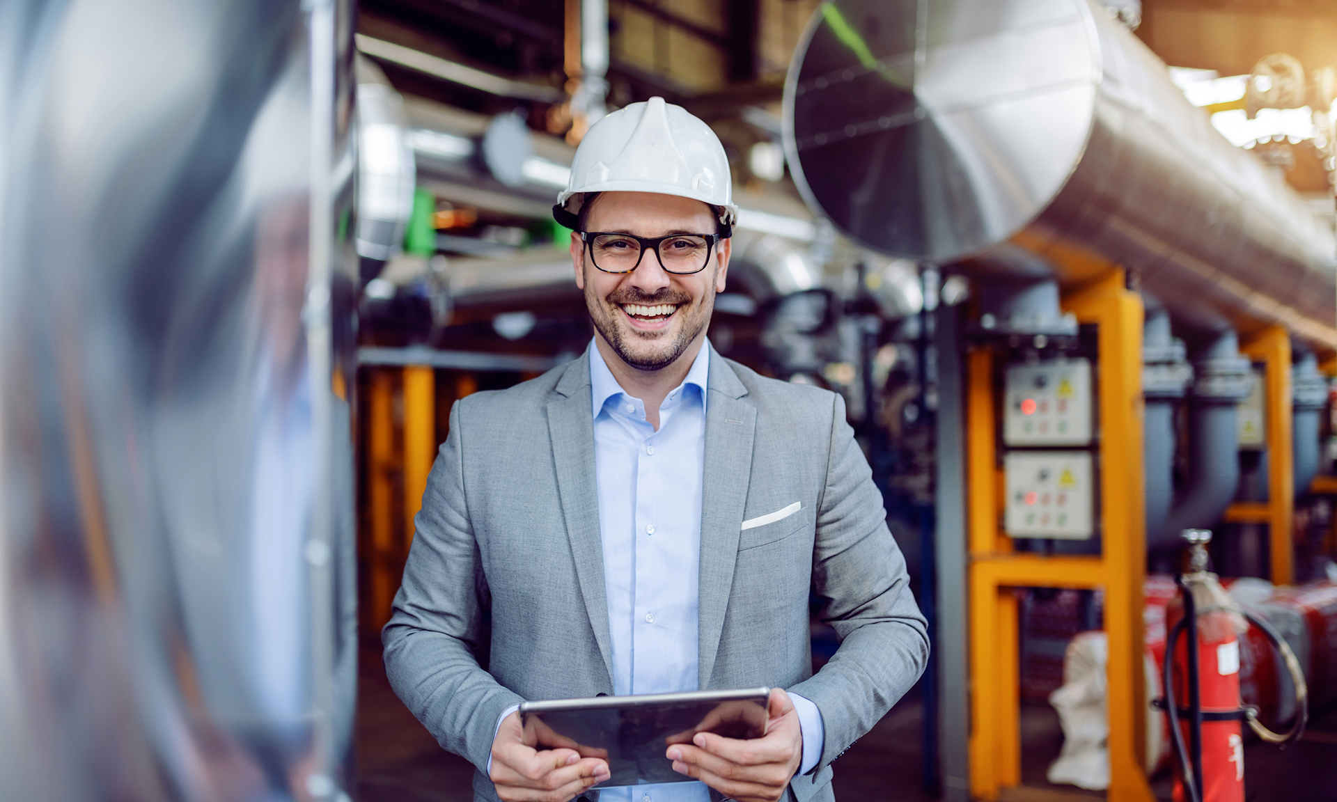 Man wearing a helmet and holding a tablet with Agentforce Manufacturing stands in a production hall and looks at the camera.