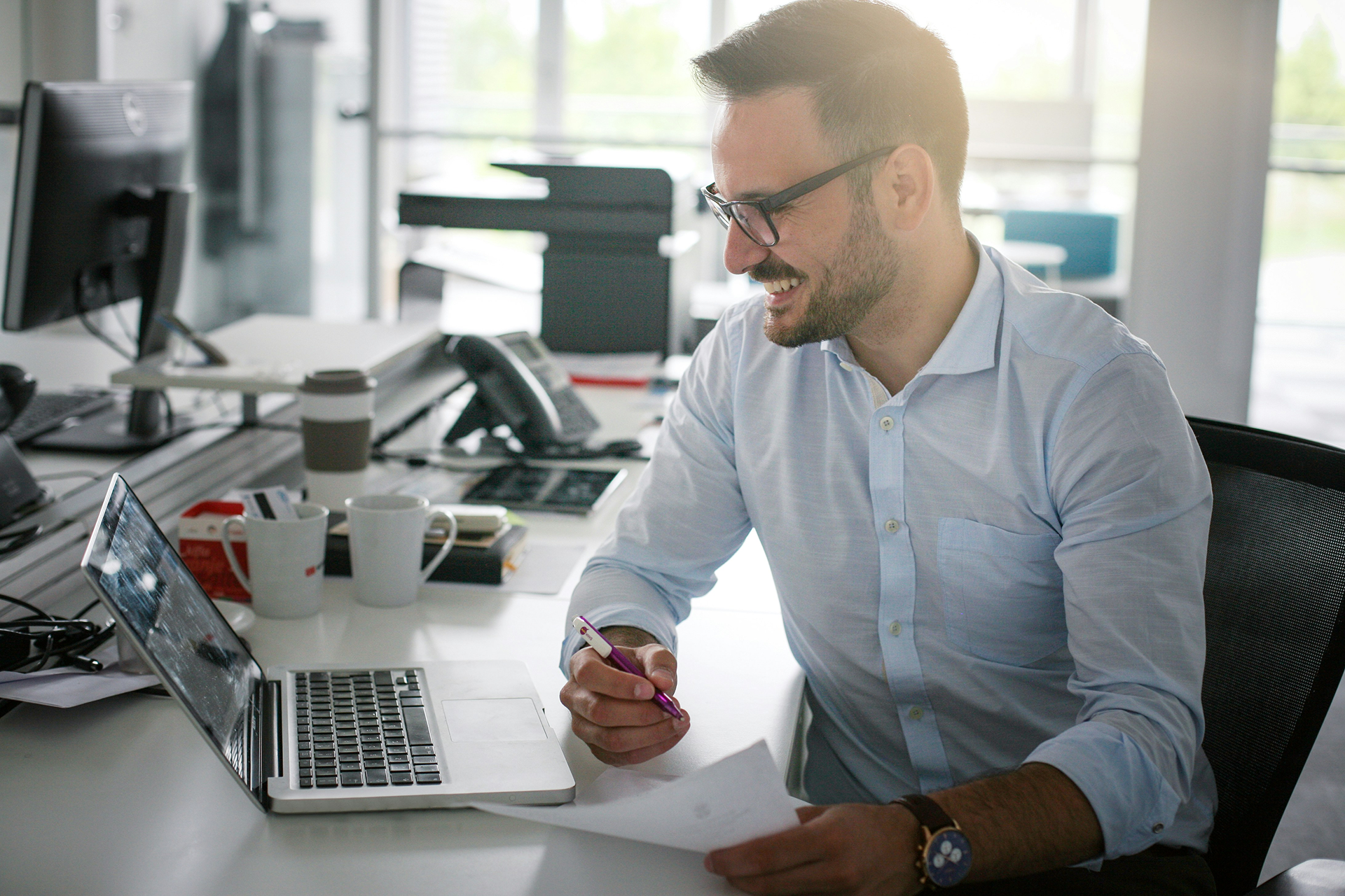 Mann sitzt an Schreibtisch vor Laptop mit Salesforce Automotive Cloud und hält Papier und Kuli.