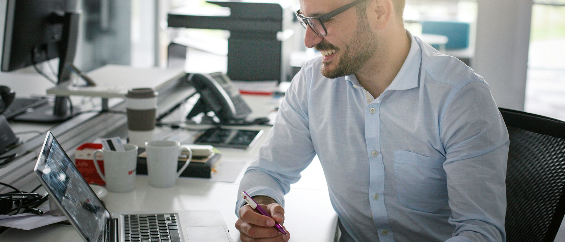 Mann sitzt an Schreibtisch vor Laptop mit Salesforce Automotive Cloud und hält Papier und Kuli.