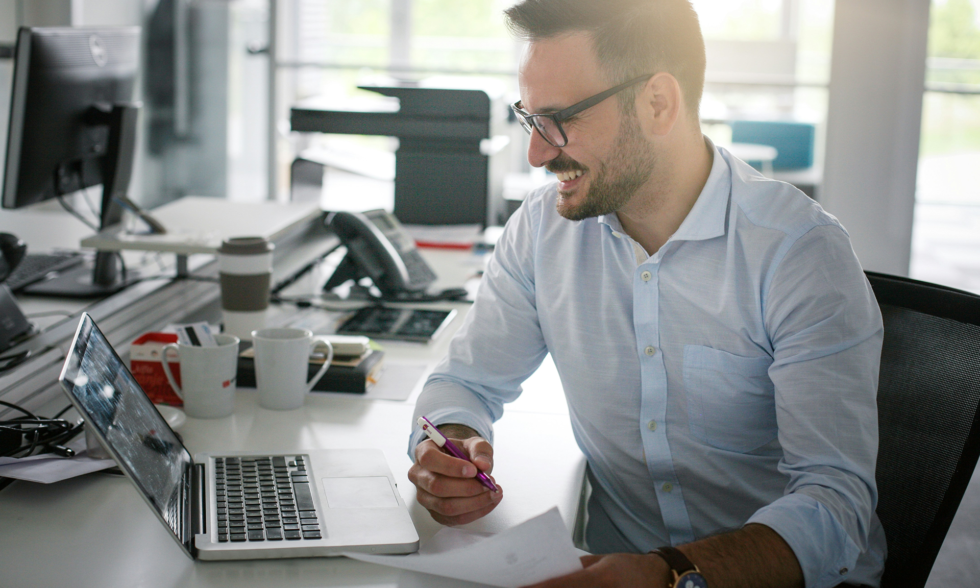 Mann sitzt an Schreibtisch vor Laptop mit Salesforce Agentforce Automotive und hält Papier und Kuli.